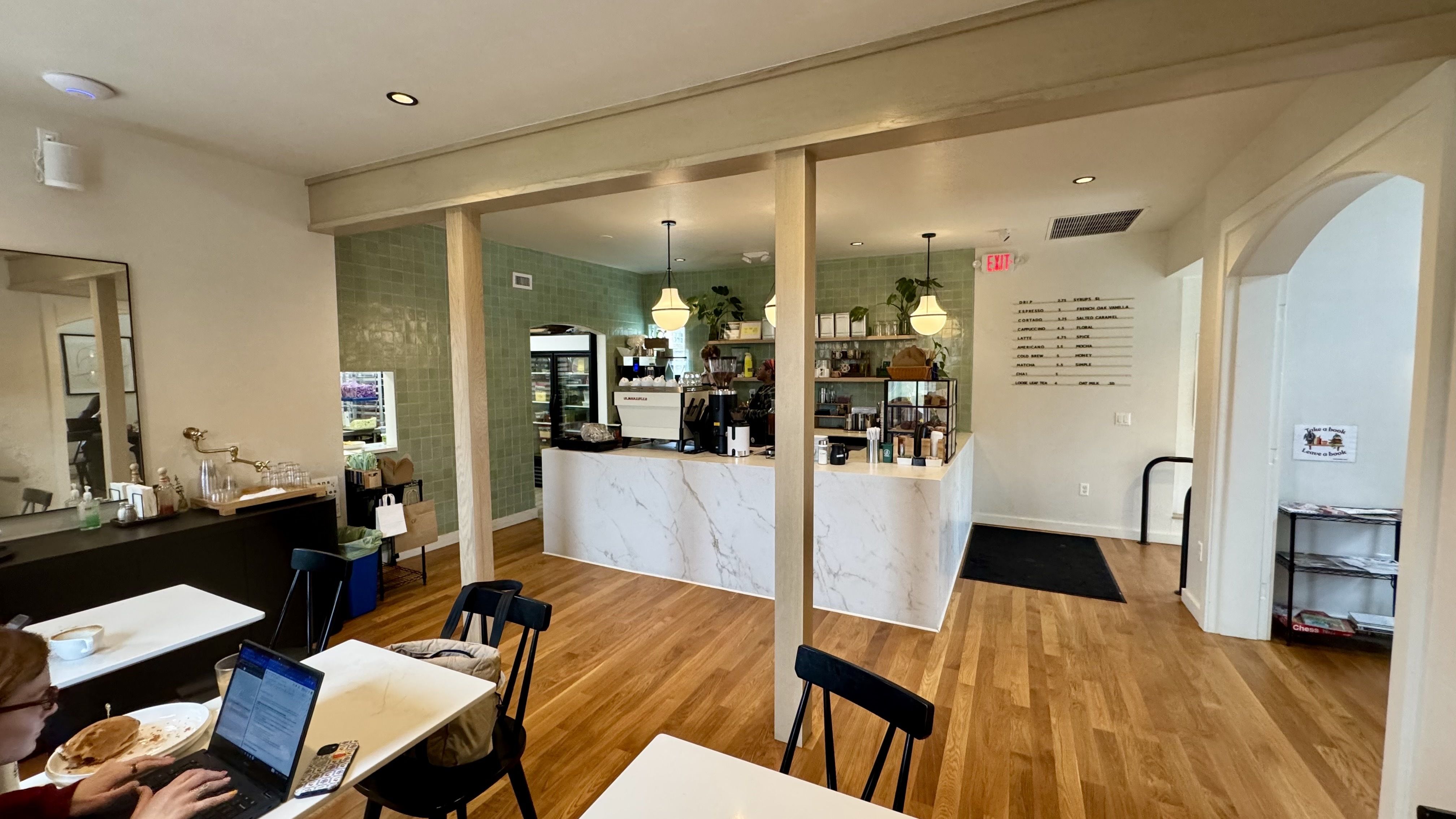 An interior cafe space with people working on laptops at tables, and some white walls and one green wall. 