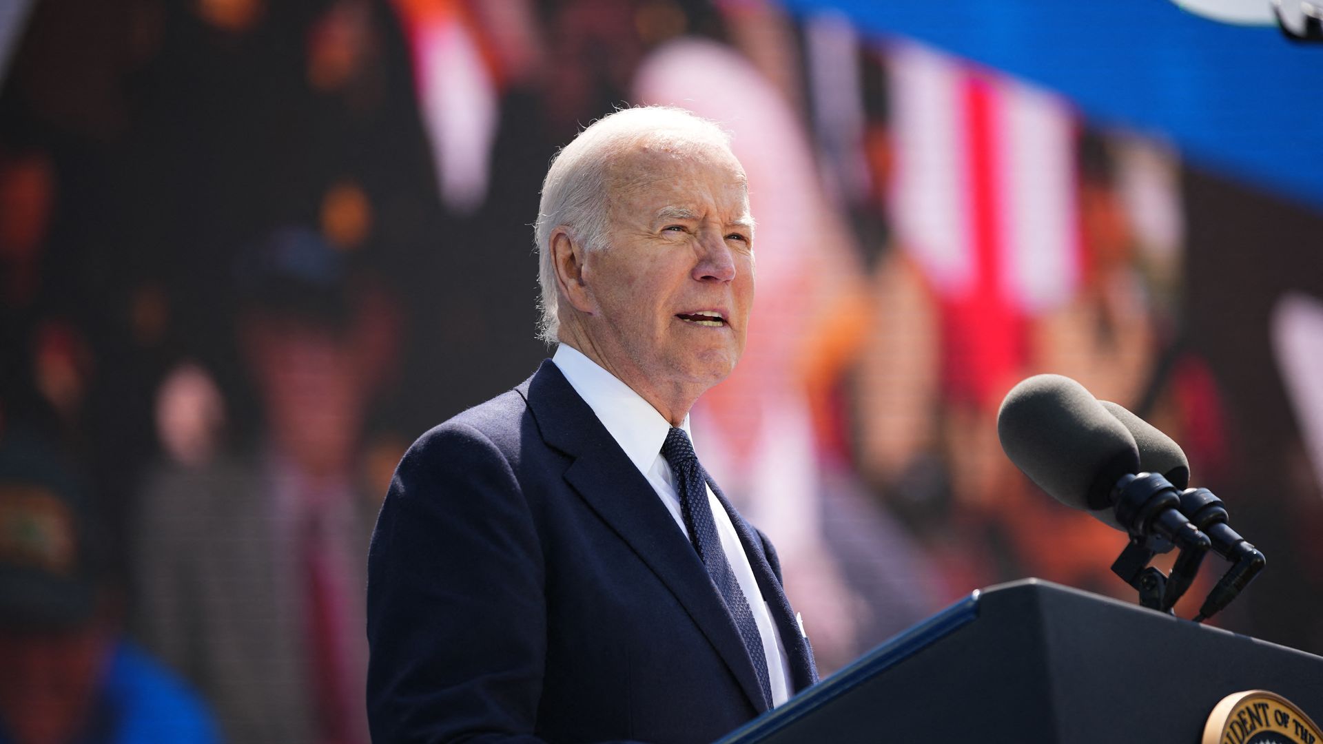 President Biden speaks behind a podium with French and American flags in the background.