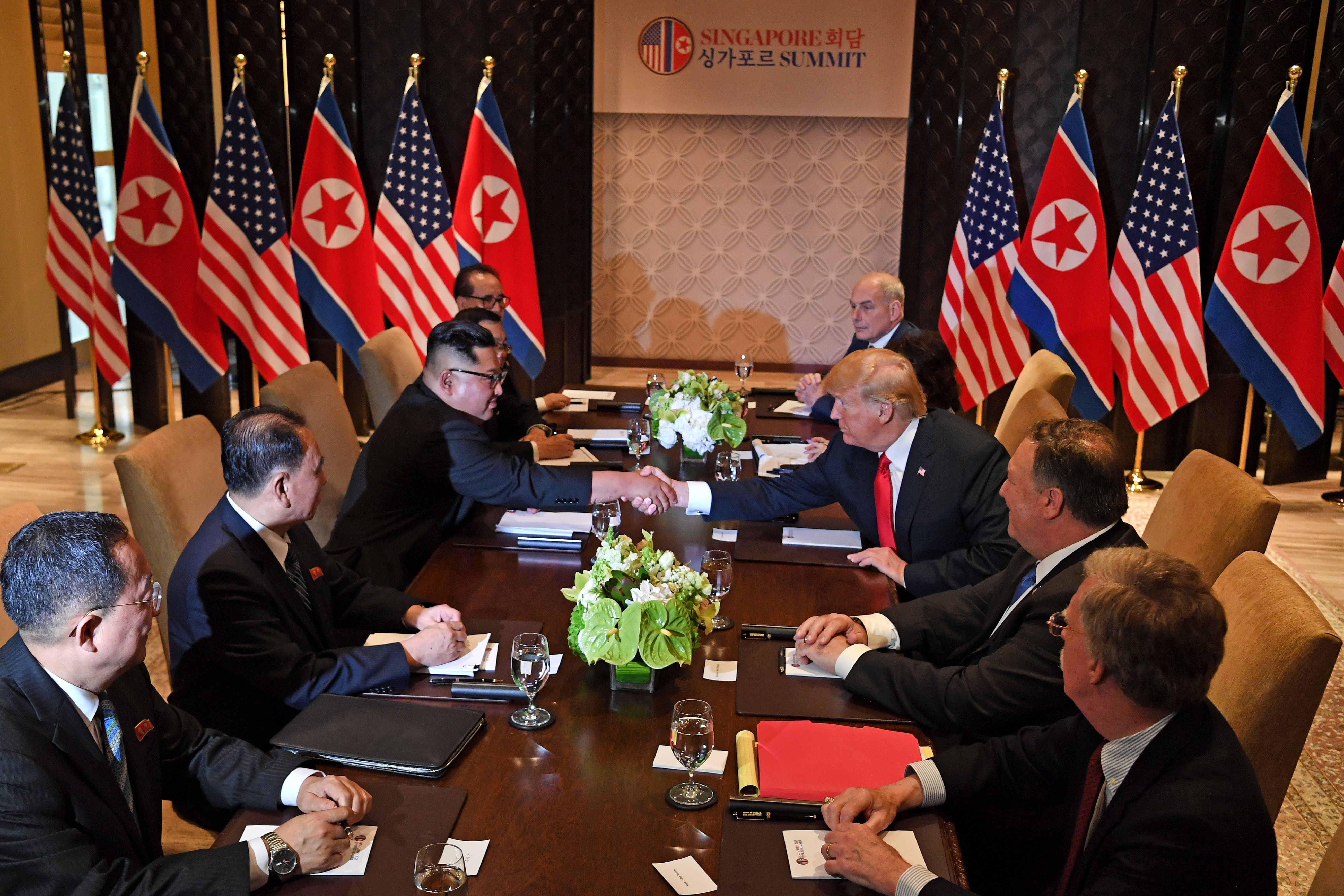 Trump and Kim shake hands across a long rectangular table