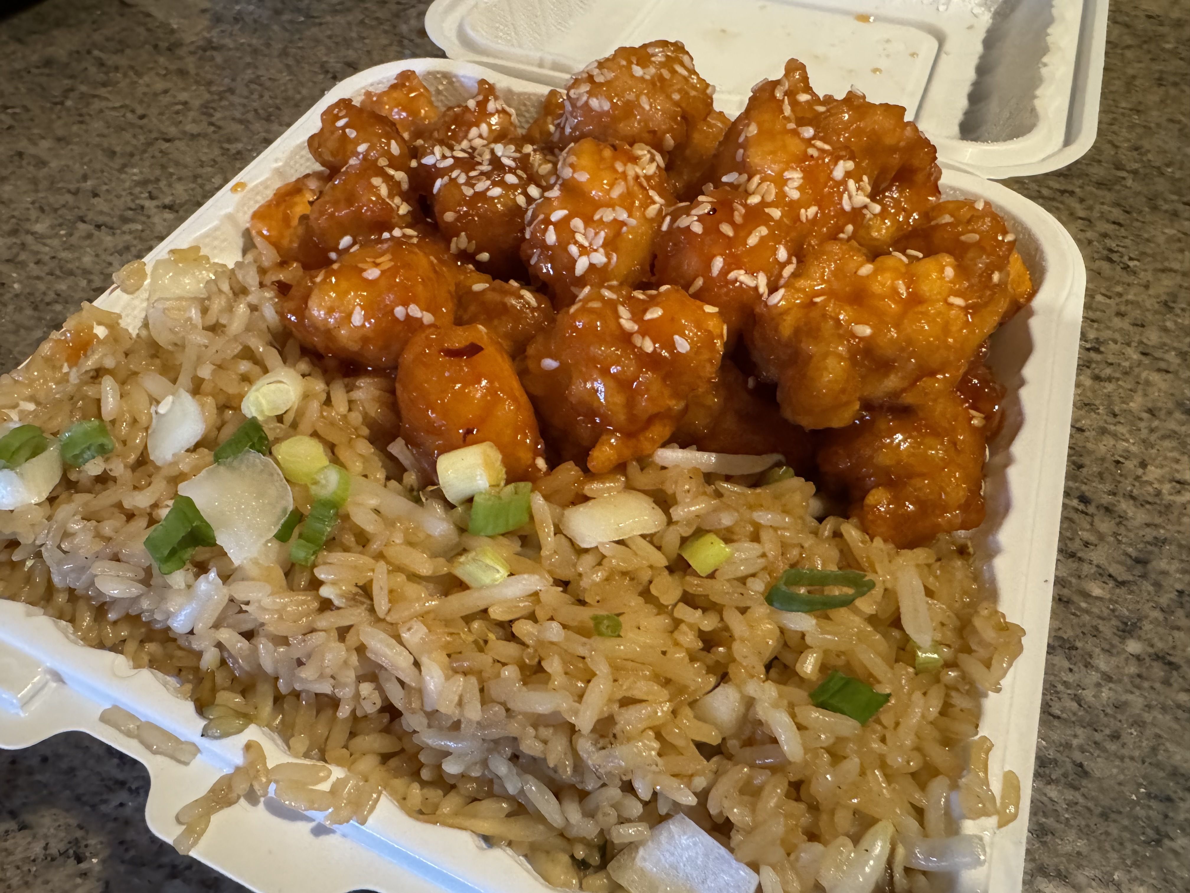 The sesame chicken and fried rice shown in a takeout container.