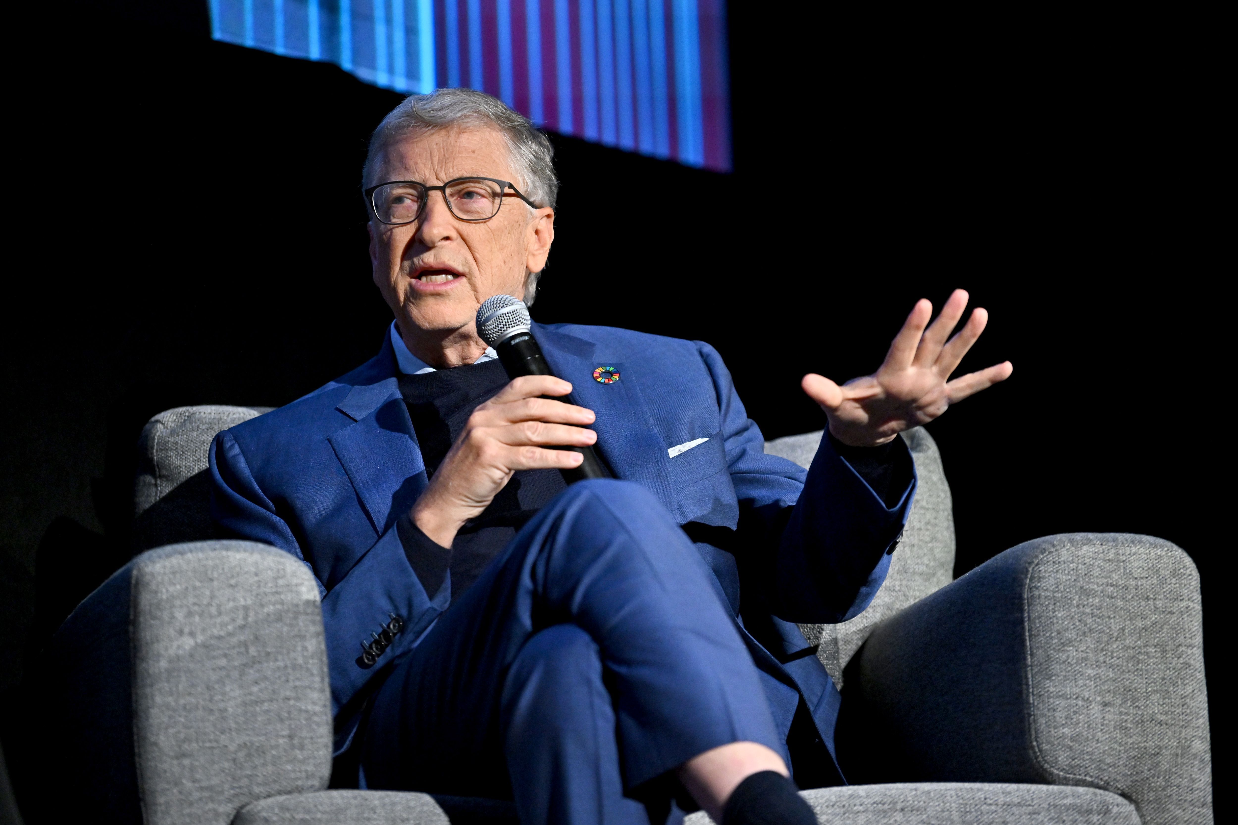 Bill Gates sitting in a gray chair with a microphone.