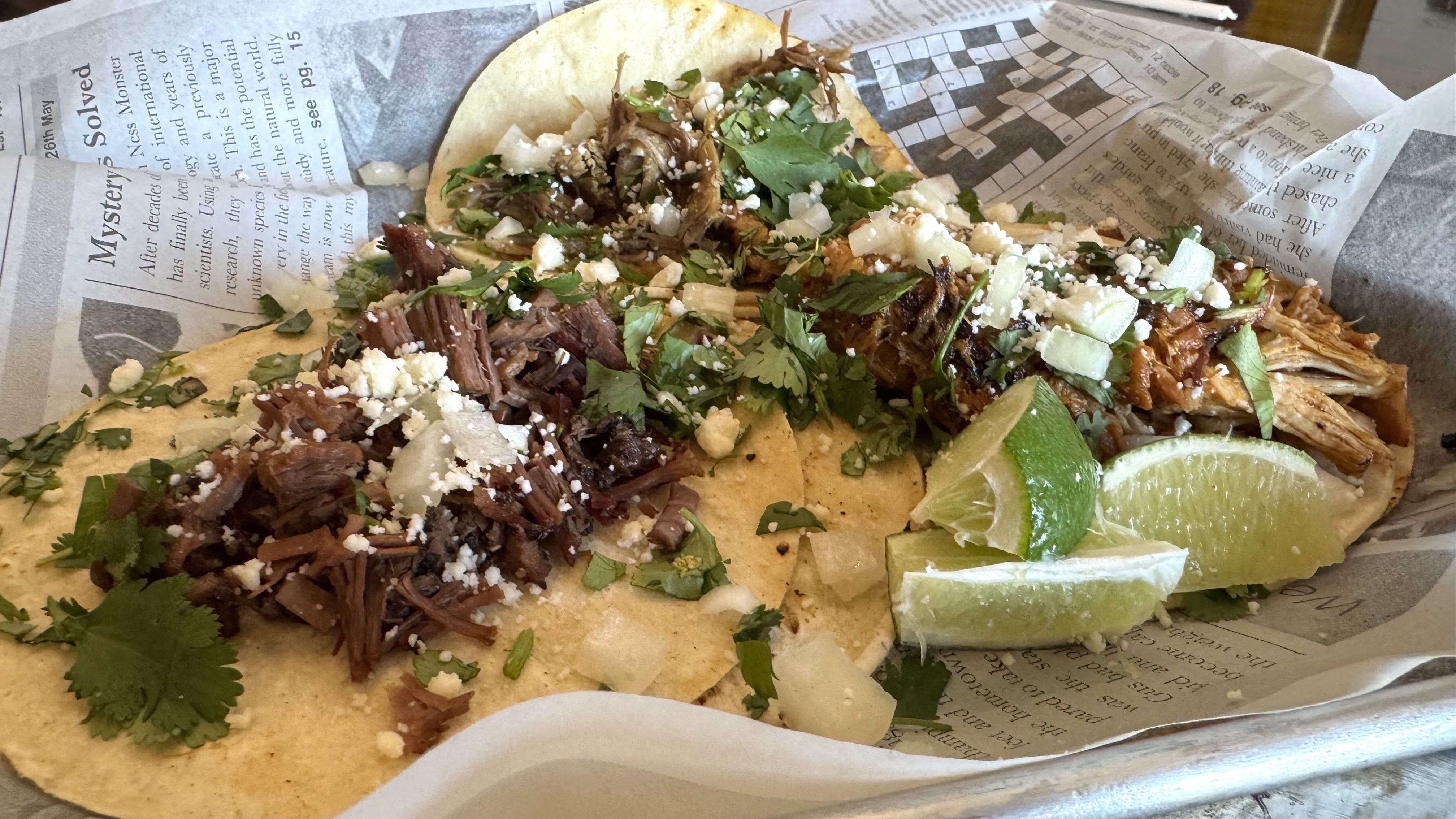A plate of three street tacos on a platter that's been covered in newsprint.