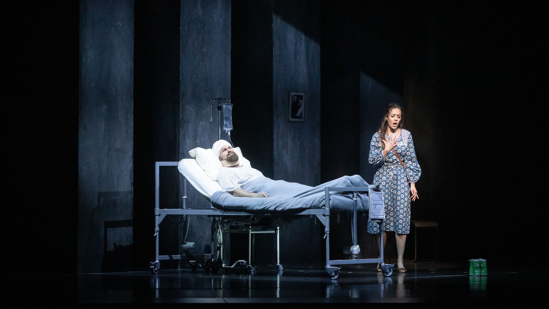 Photo of a man in a hospital bed and a woman in a dress standing by the bed, singing.