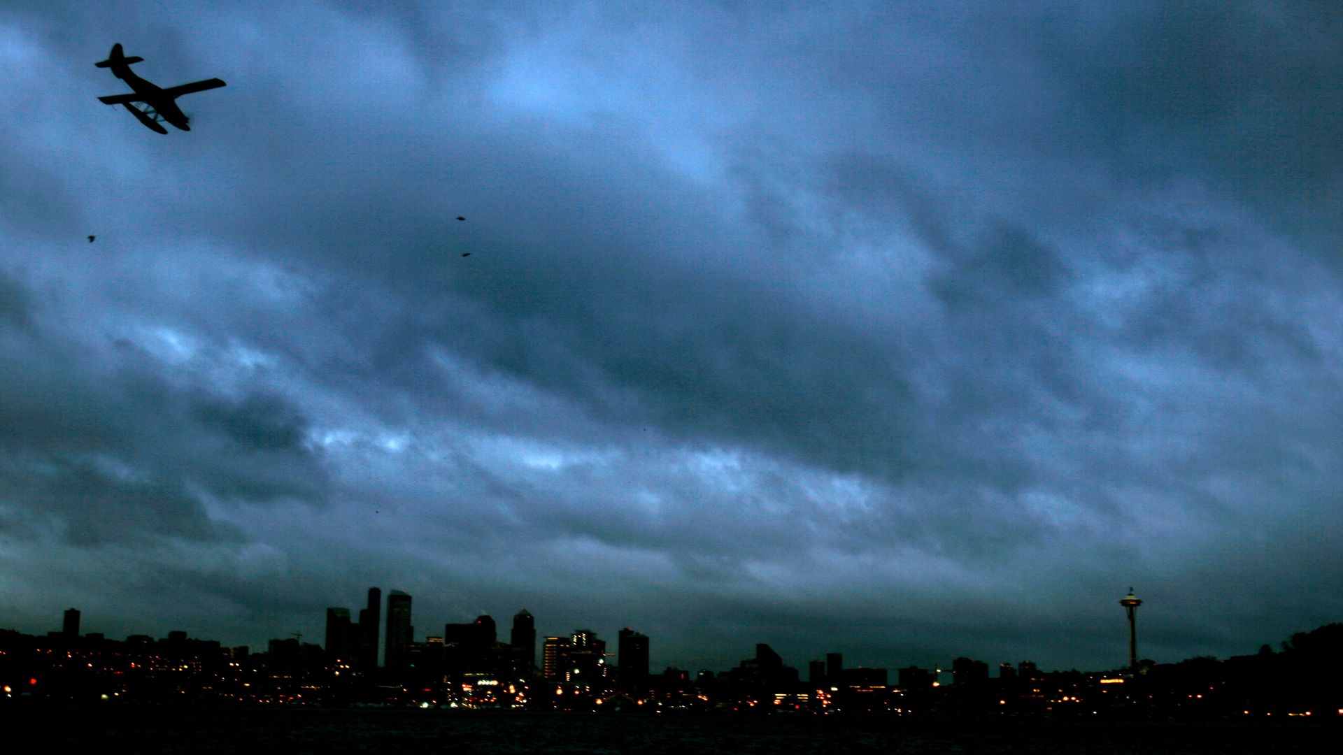 A plane flies among thick dark clouds over Seattle. 
