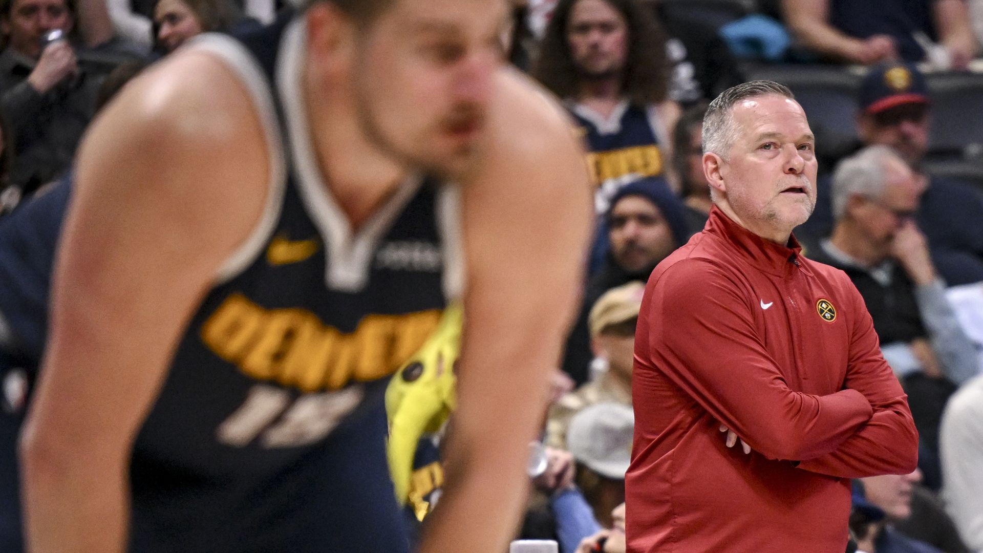 A man in a red jacket stands with his arms folded. 