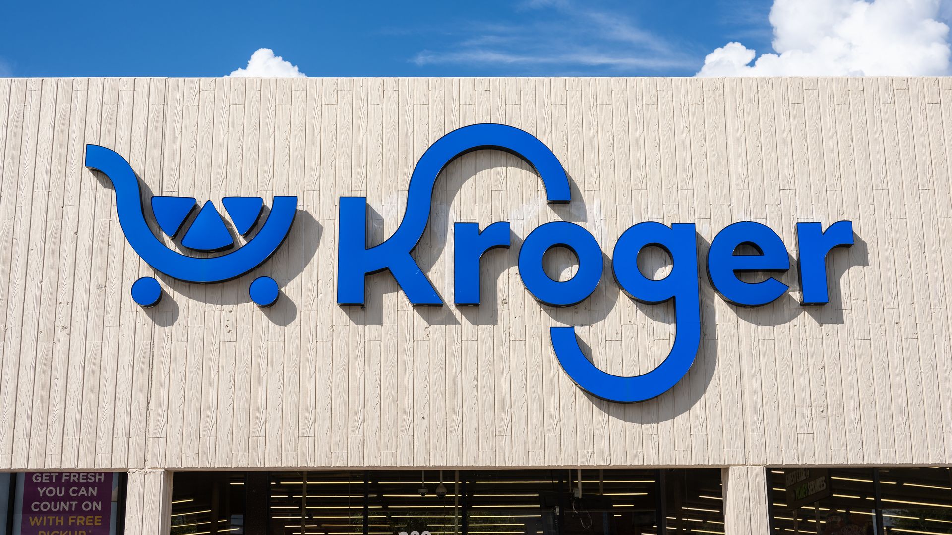 Kroger store with blue Krogre logo on white stone building. Blue sky with clouds in the background.