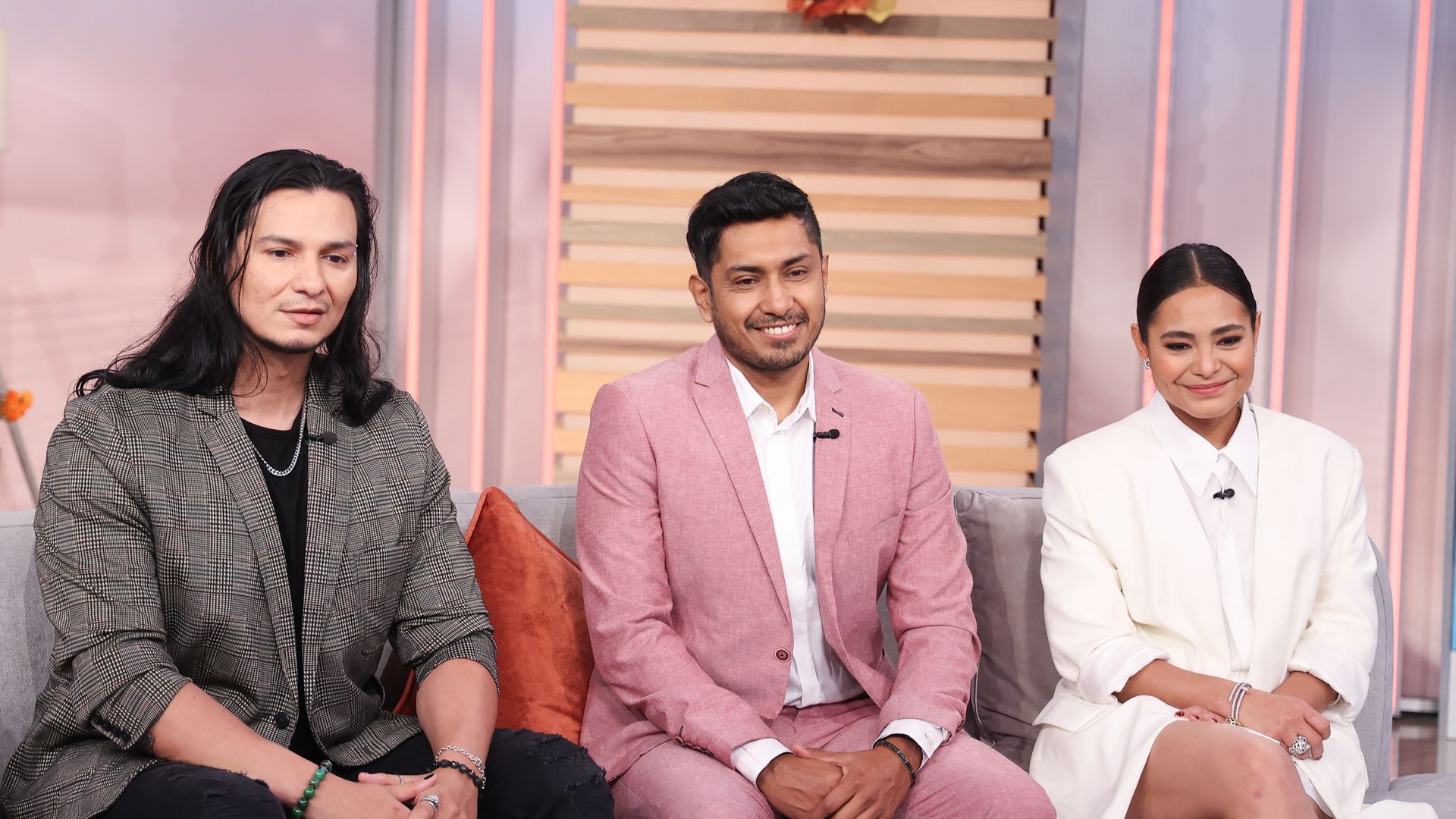 Alex Livinalli, Tenoch Huerta and Mabel Cadena sit on a sofa, smiling while looking down, while at "Despierta America" at Univision Studios to promote Wakanda Forever 