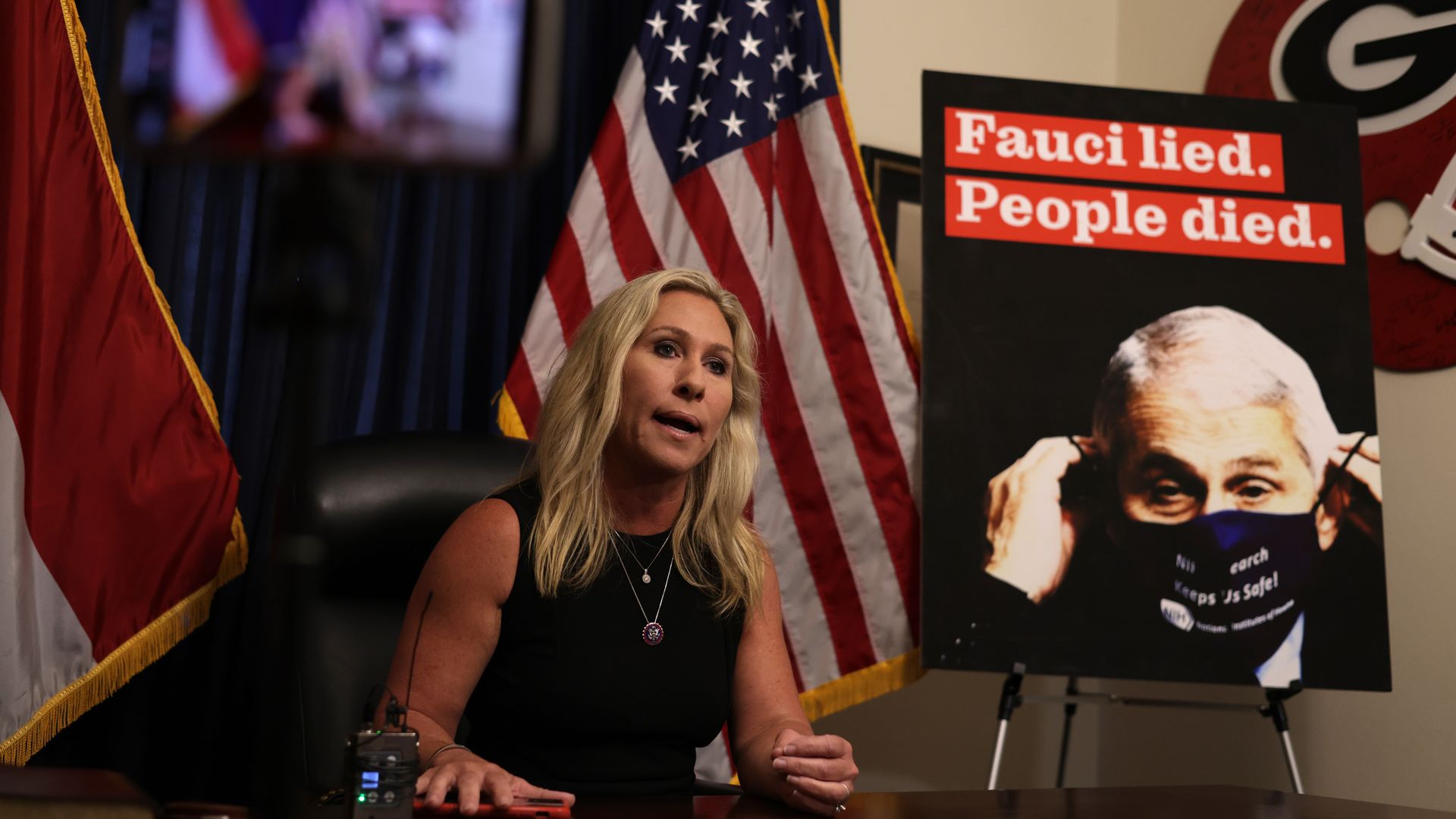 Marjorie Taylor Greene at a press conference in front of a "Fauci lied" poster