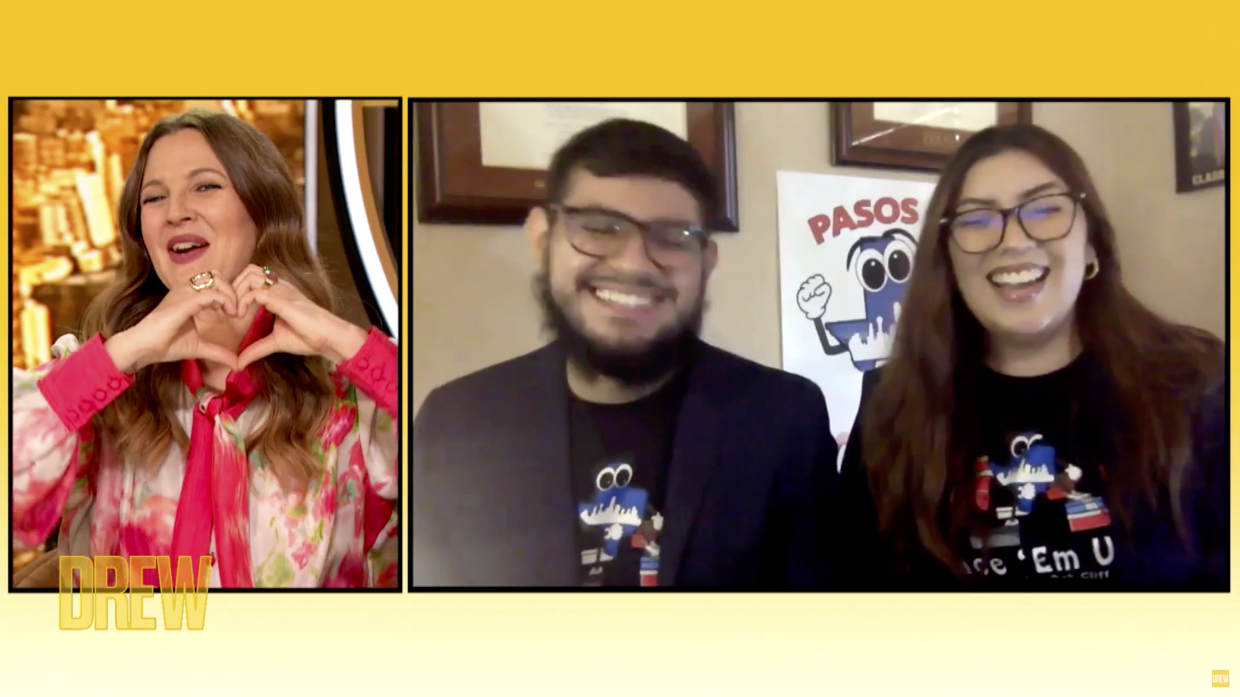 Three people smiling in a video call frame with yellow border; left woman wears floral pink blouse making a heart with hands; right two wear glasses, black shirts and are laughing.
