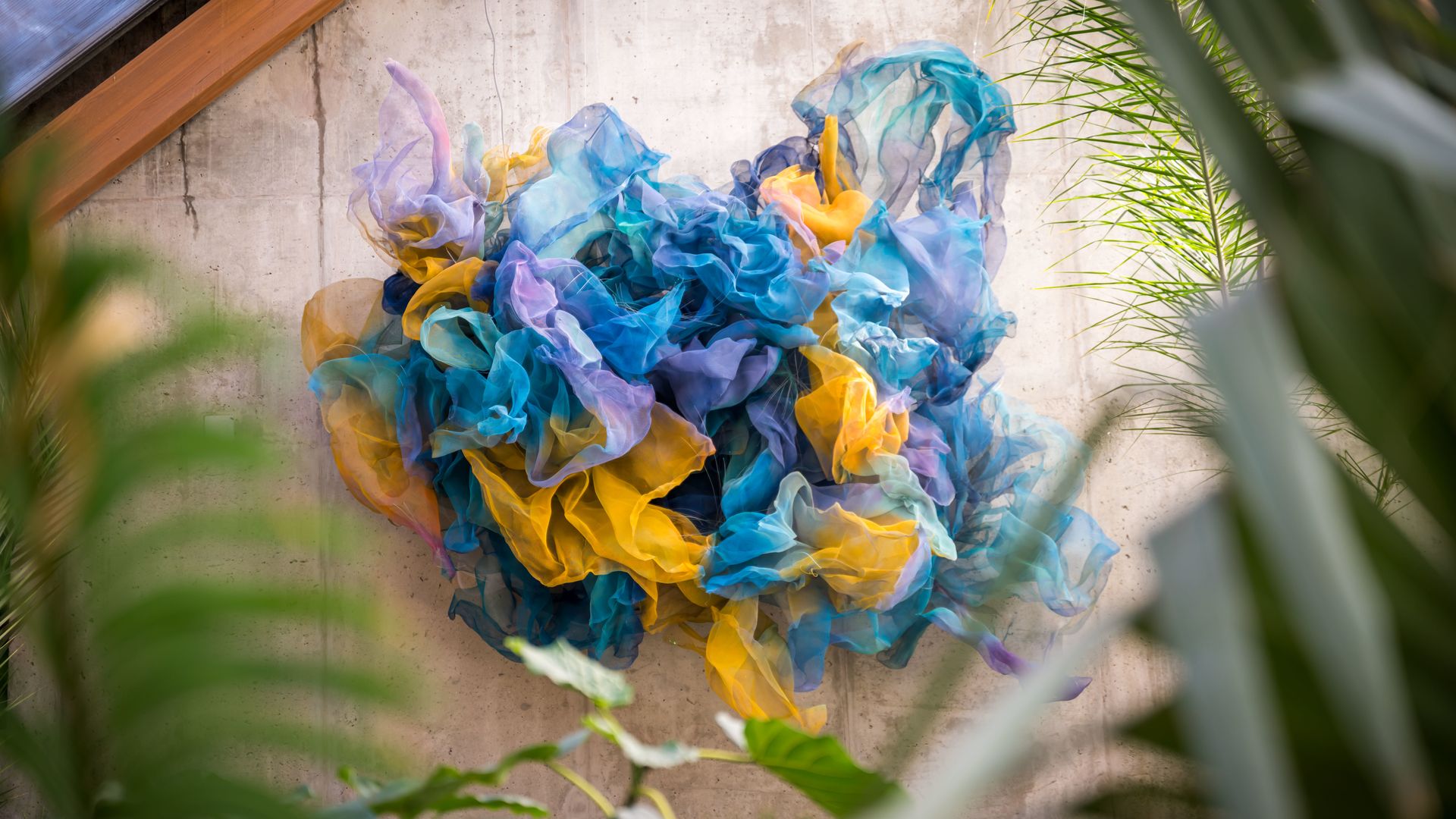 An aerial sculpture features flowy materials in several colors, including mustard yellow, light purple and light blue, as part of the New England Botanical Garden's annual orchid exhibition.
