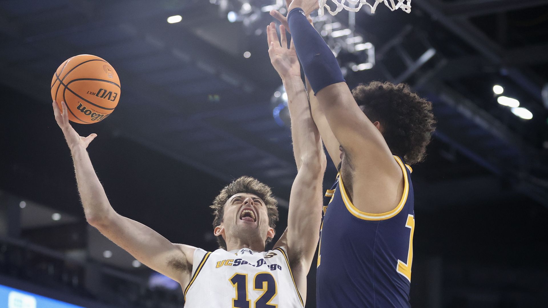 A basketball players goes up for a layup against a defender.