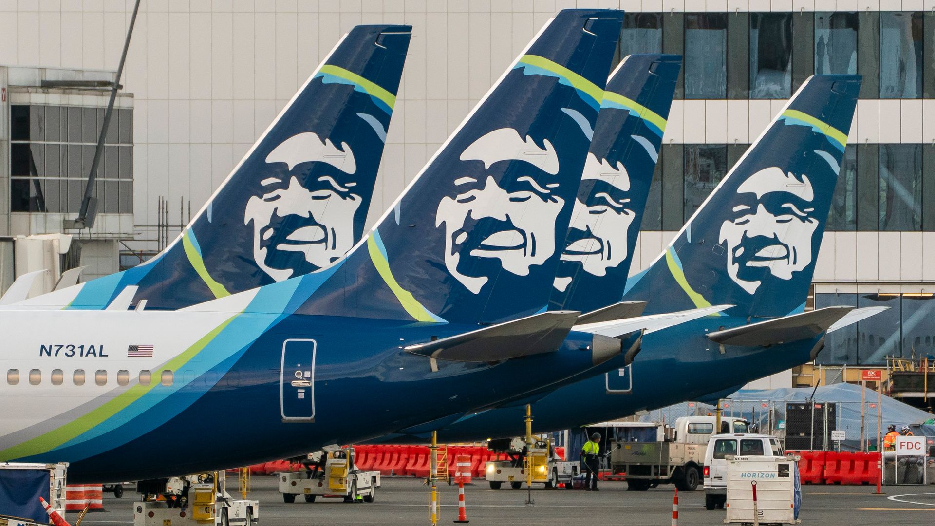 Alaska Airlines planes sit at gates at Seattle-Tacoma International Airport as ground crews work on the tarmac.