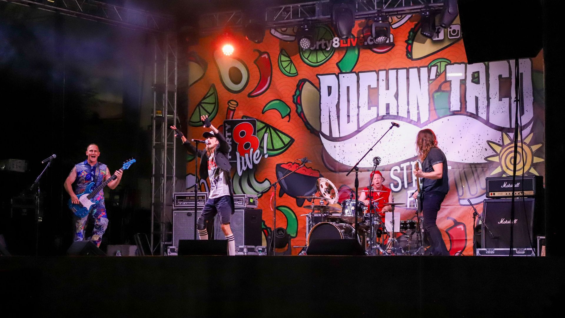A band performing with a sign that says, "Rockin' Taco" in the background. 