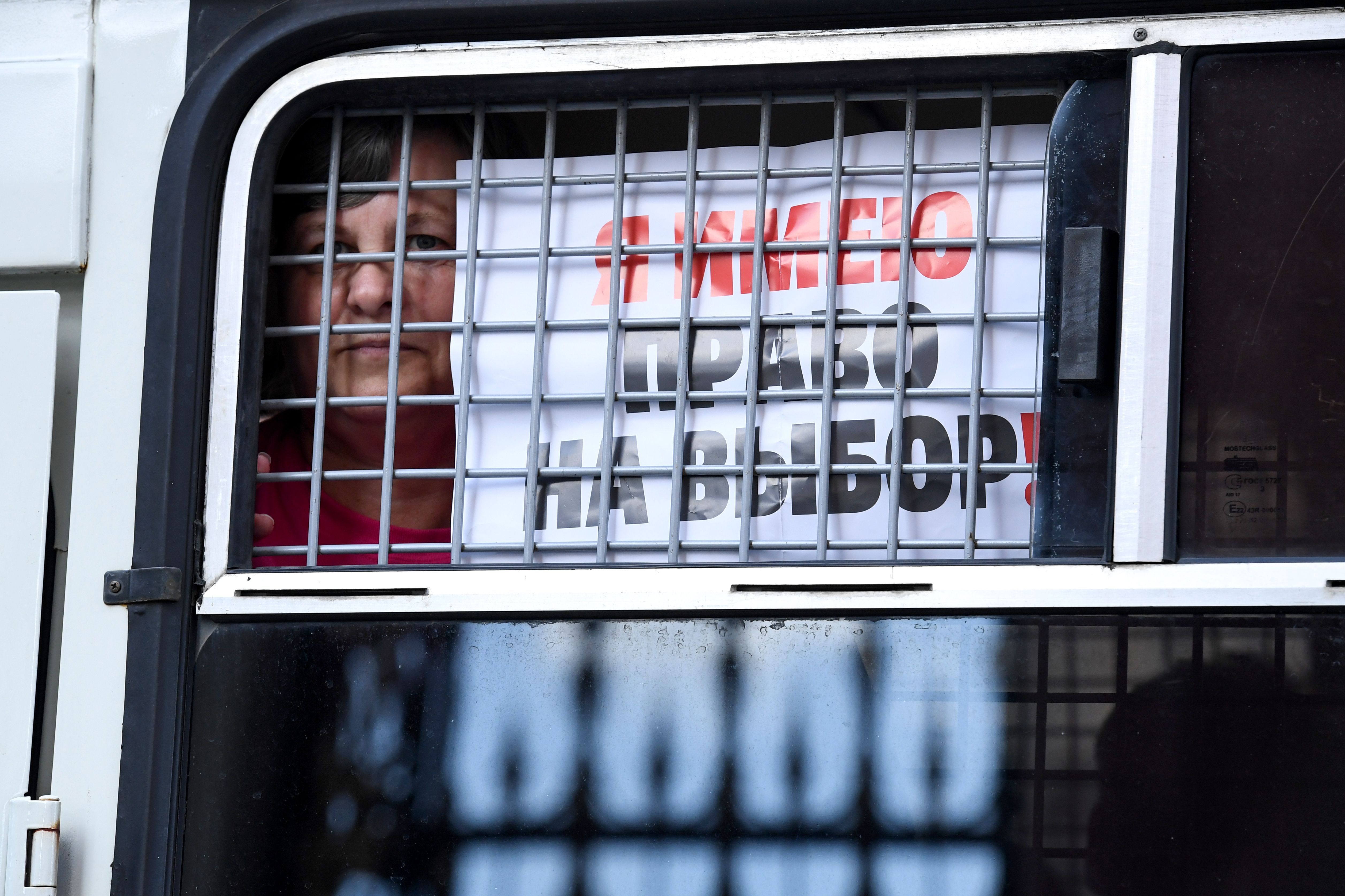 A detained protester shows the placard reading "I have the right to choose" from the window of a police bus.