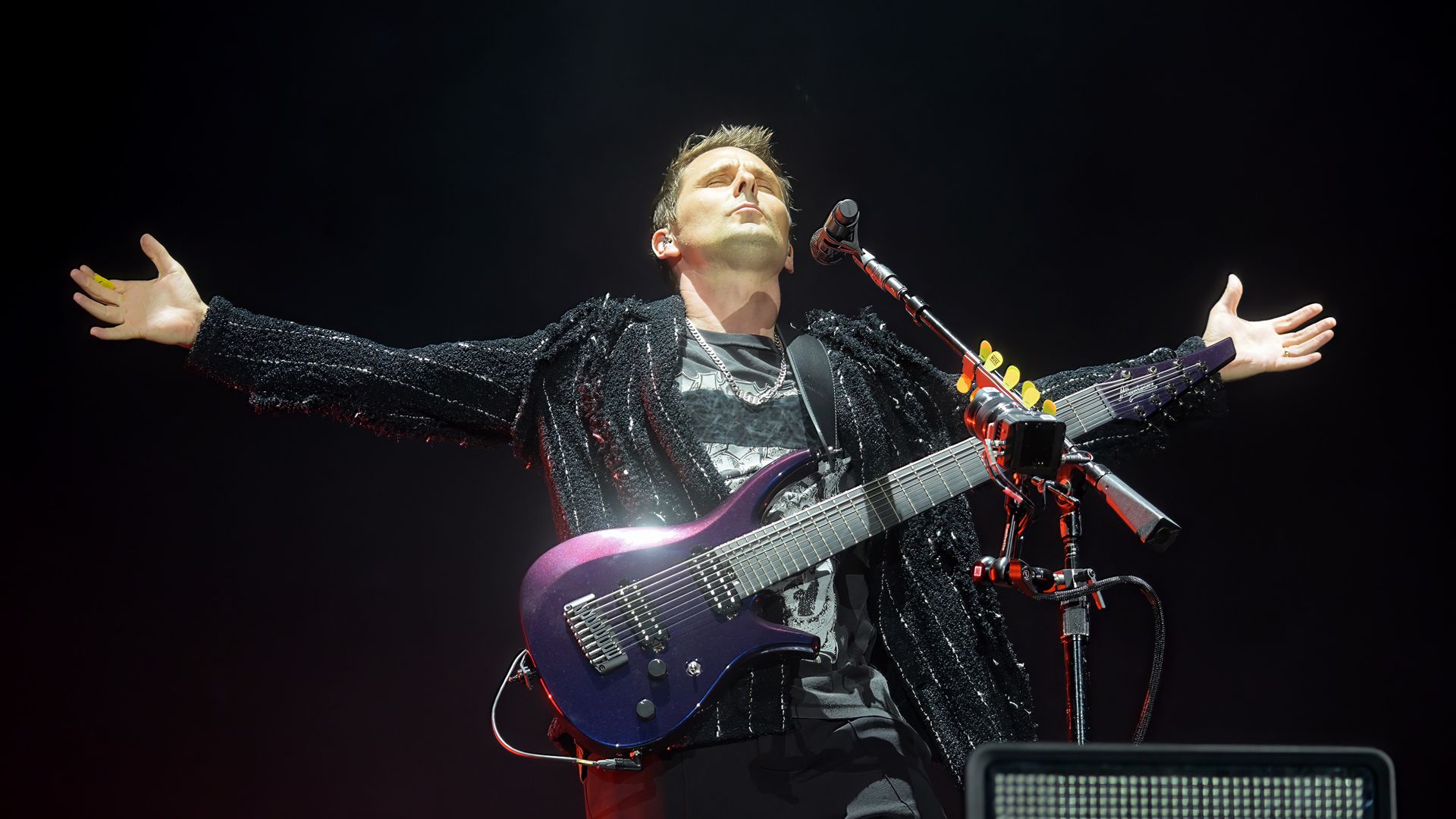 Muse guitarist Matt Bellamy on stage holding a guitar and his arms are outstretched. 