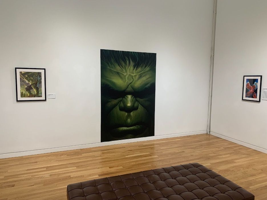 A large painting of the Incredible Hulk takes up the majority of a white blank wall, next two two smaller Marvel artworks.