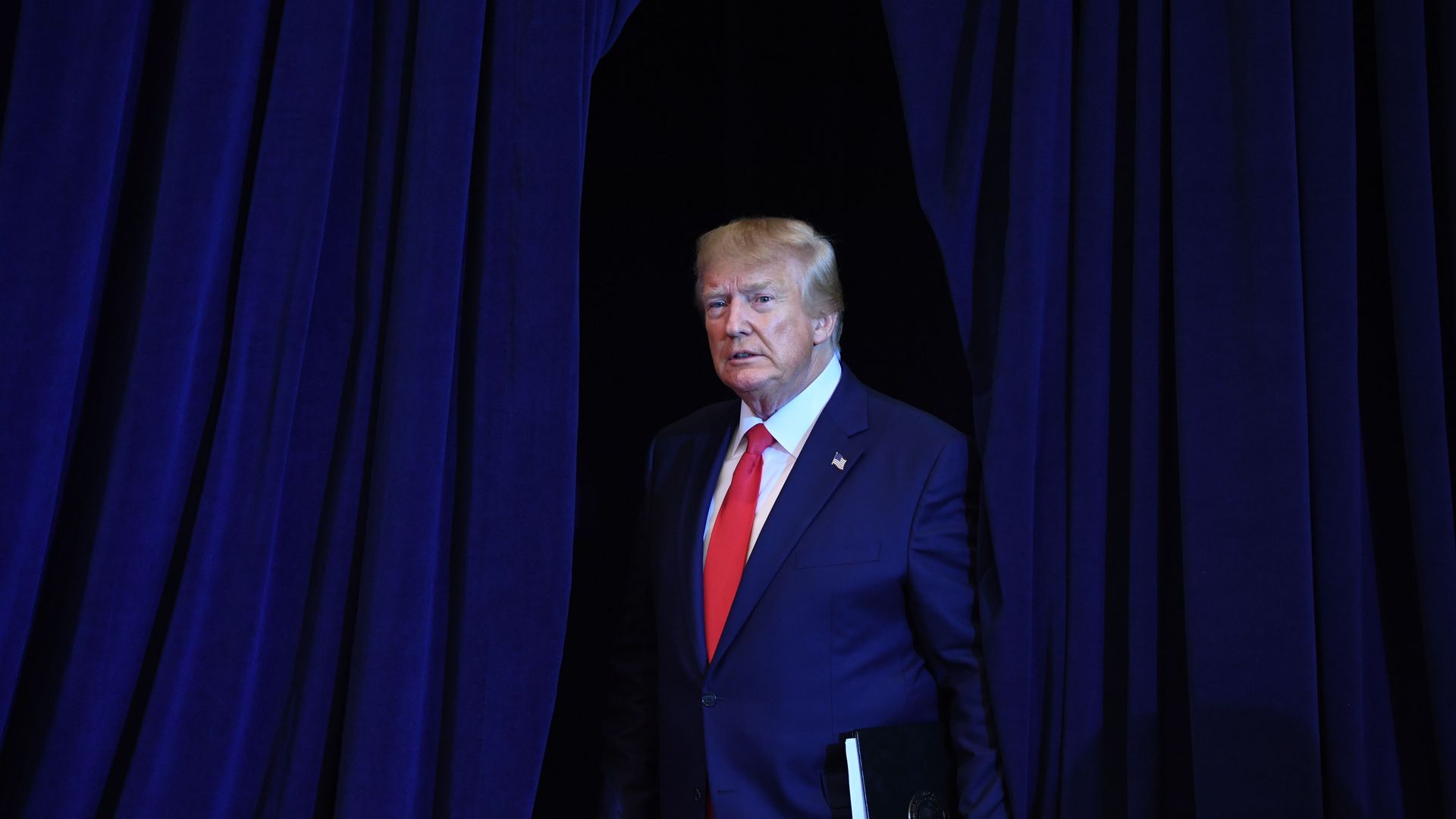 Photo of Donald Trump in a blue suit and red tie, against a dark navy blue backdrop