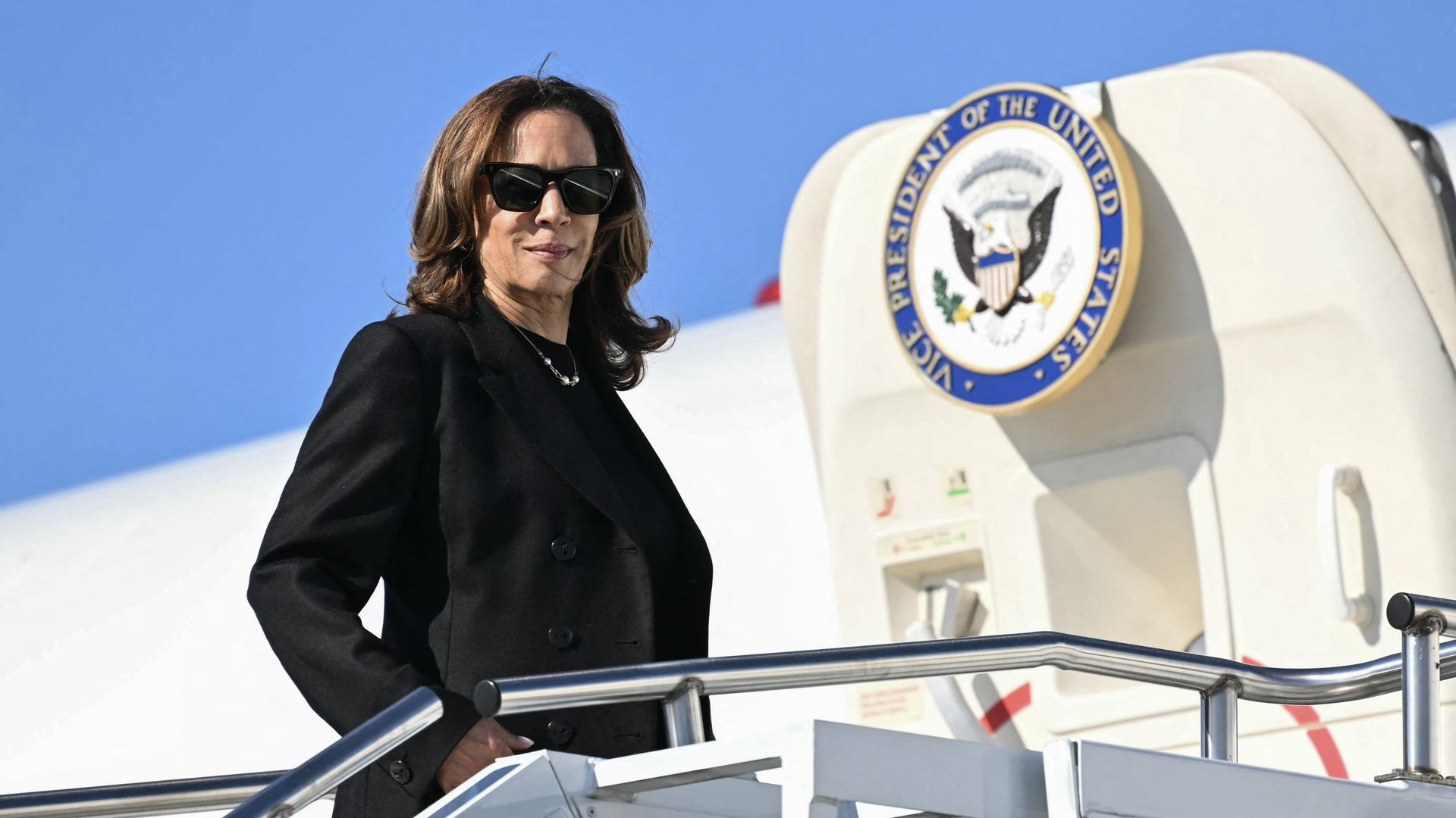 Vice President Harris, wearing a dark gray suit and standing outside a white plane with the vice presidential seal on it.