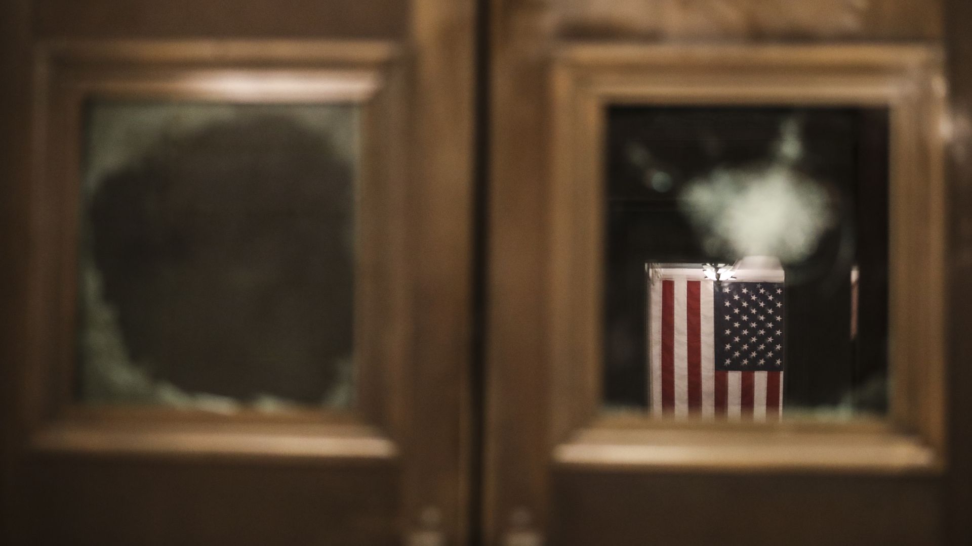 A picture of a door near the Capitol rotunda with glass panels broken and a US flag in the background
