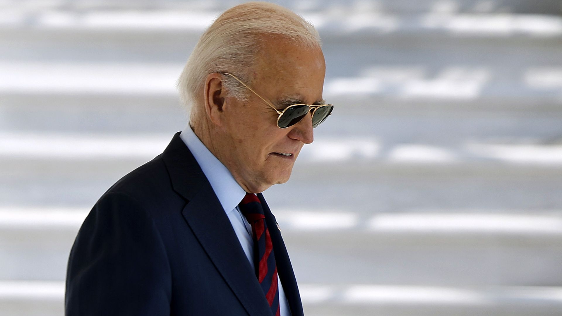 President Biden, in a blue suit, blue shirt and blue- and red-striped tie, and wearing sunglasses.