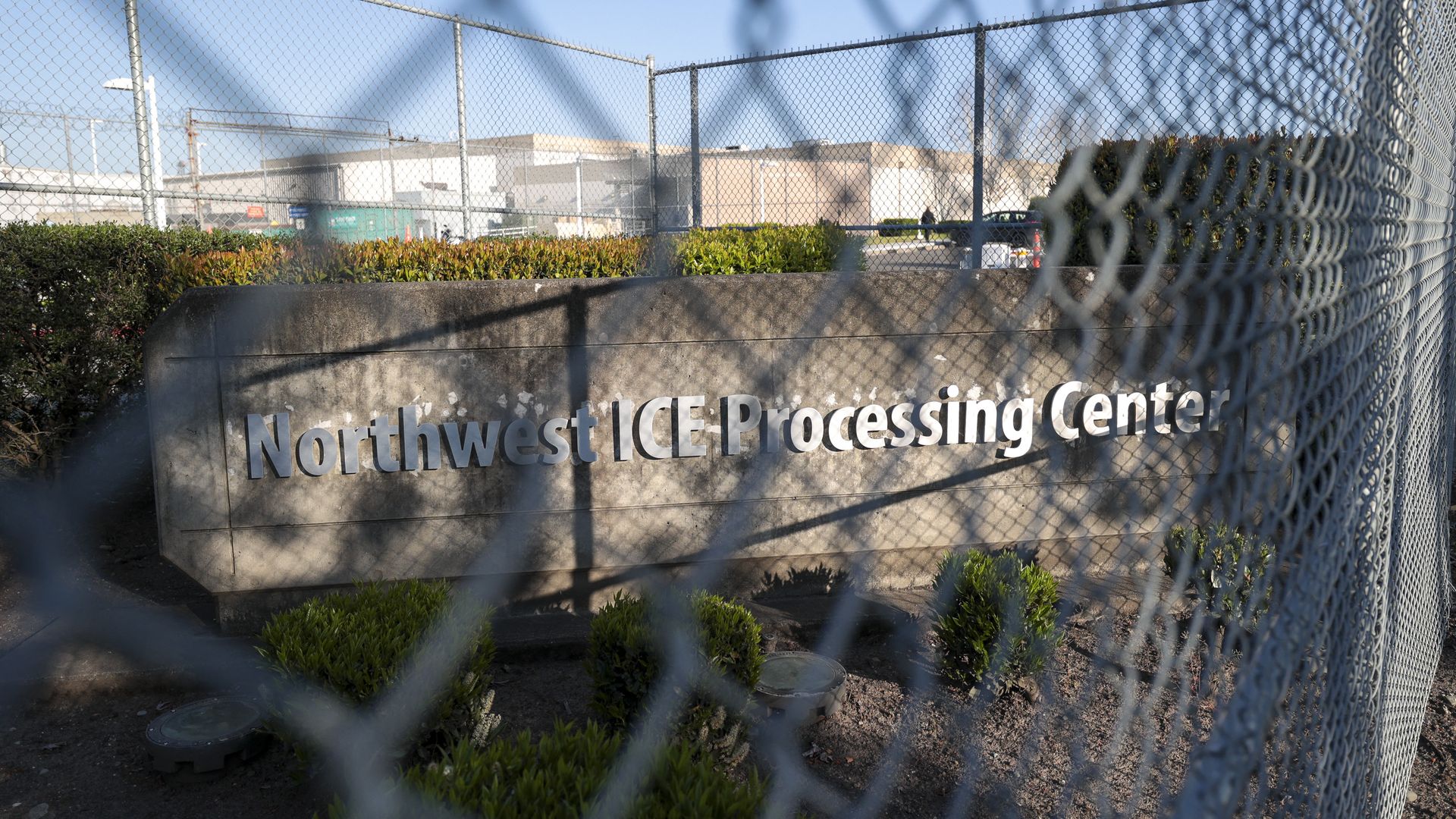 A chainlink fence sits in front of a sign that says "Northwest ICE Processing Center"