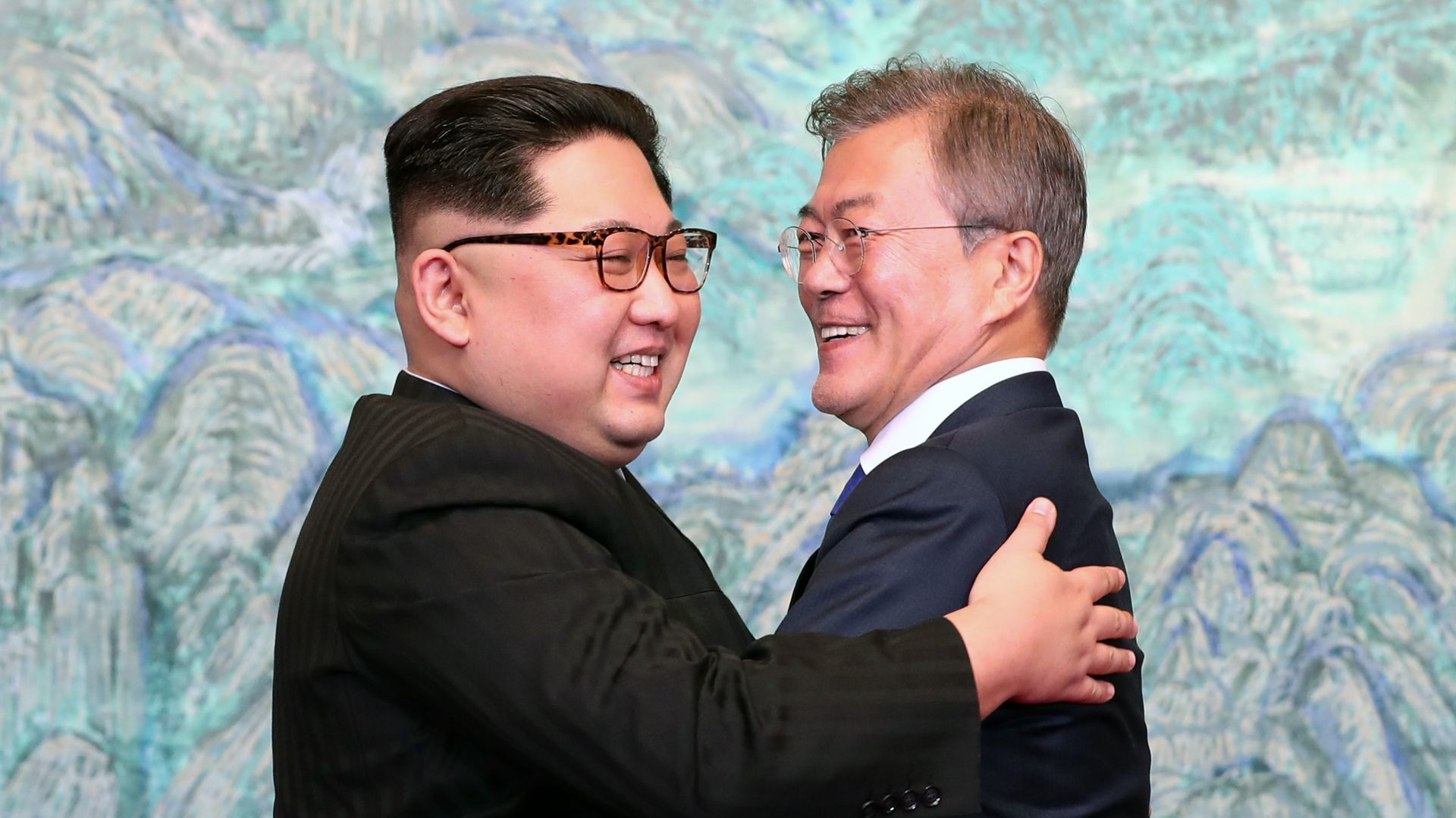 Kim Jong-un ad Moon Jae-in embrace before a blue-green background.