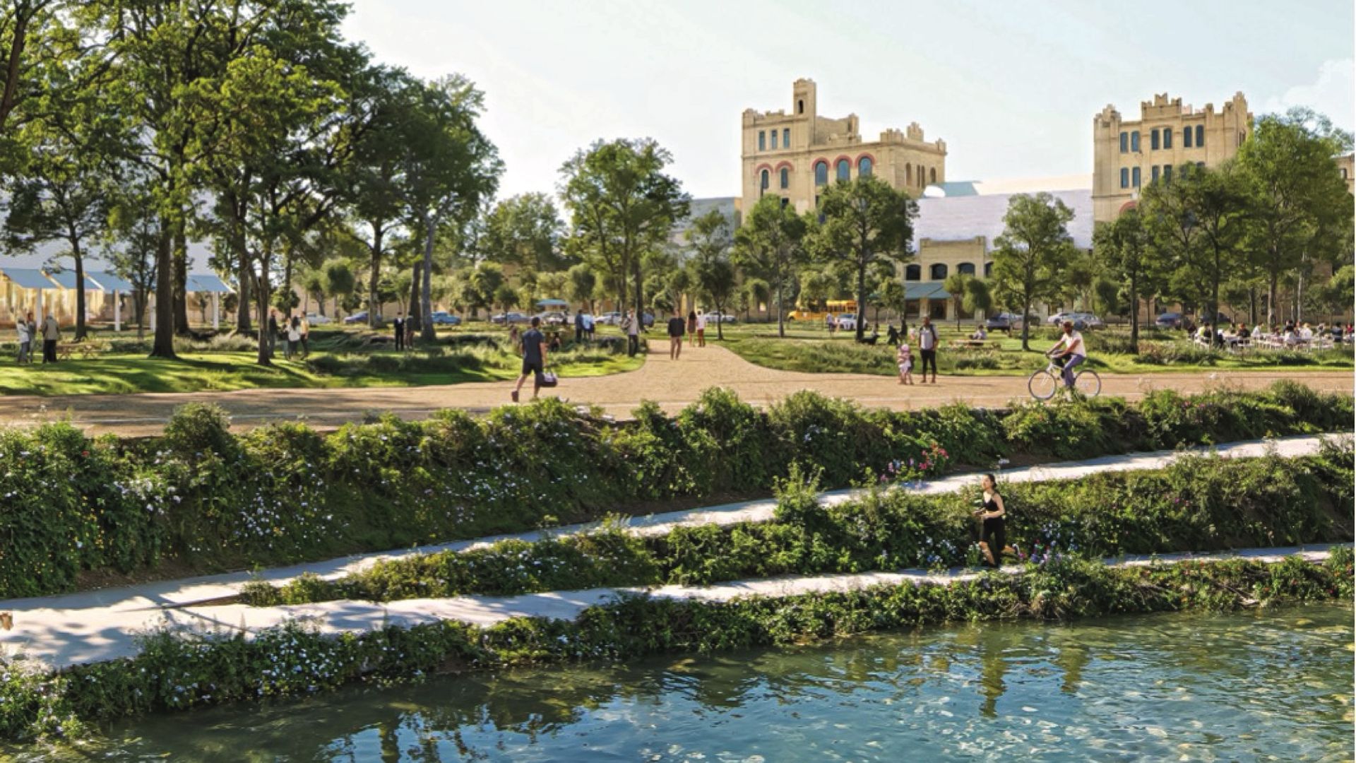 A sunlit park area and the San Antonio River sit in front of the San Antonio Museum of Art. Trees and greenery line a walking path and people walk and bike around.