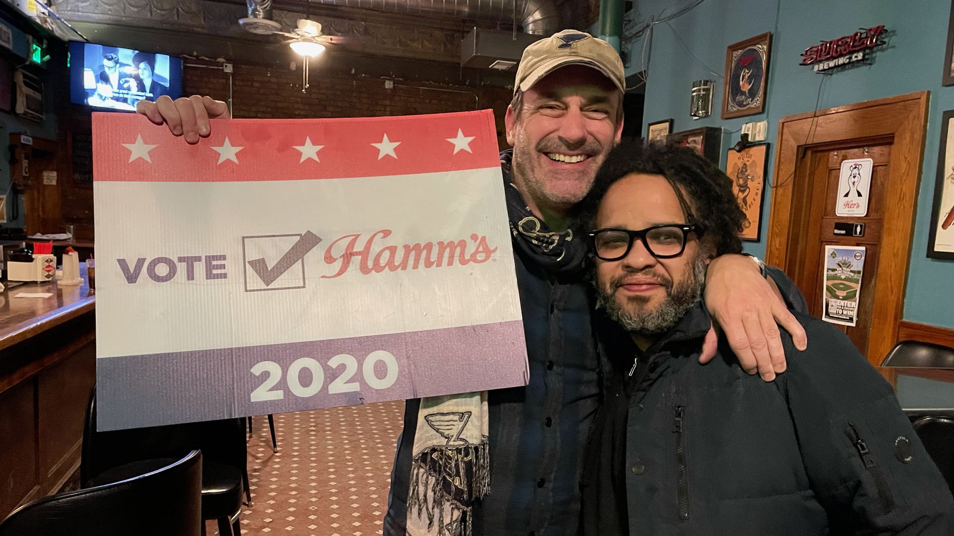 Jon Hamm and Tony Zaccardi stand holding a Hamm's beer sign 