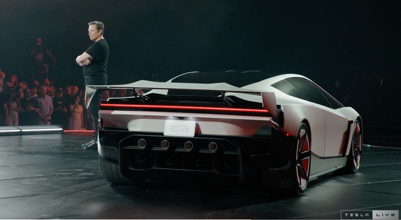 A mad on a stage stands next to a car.