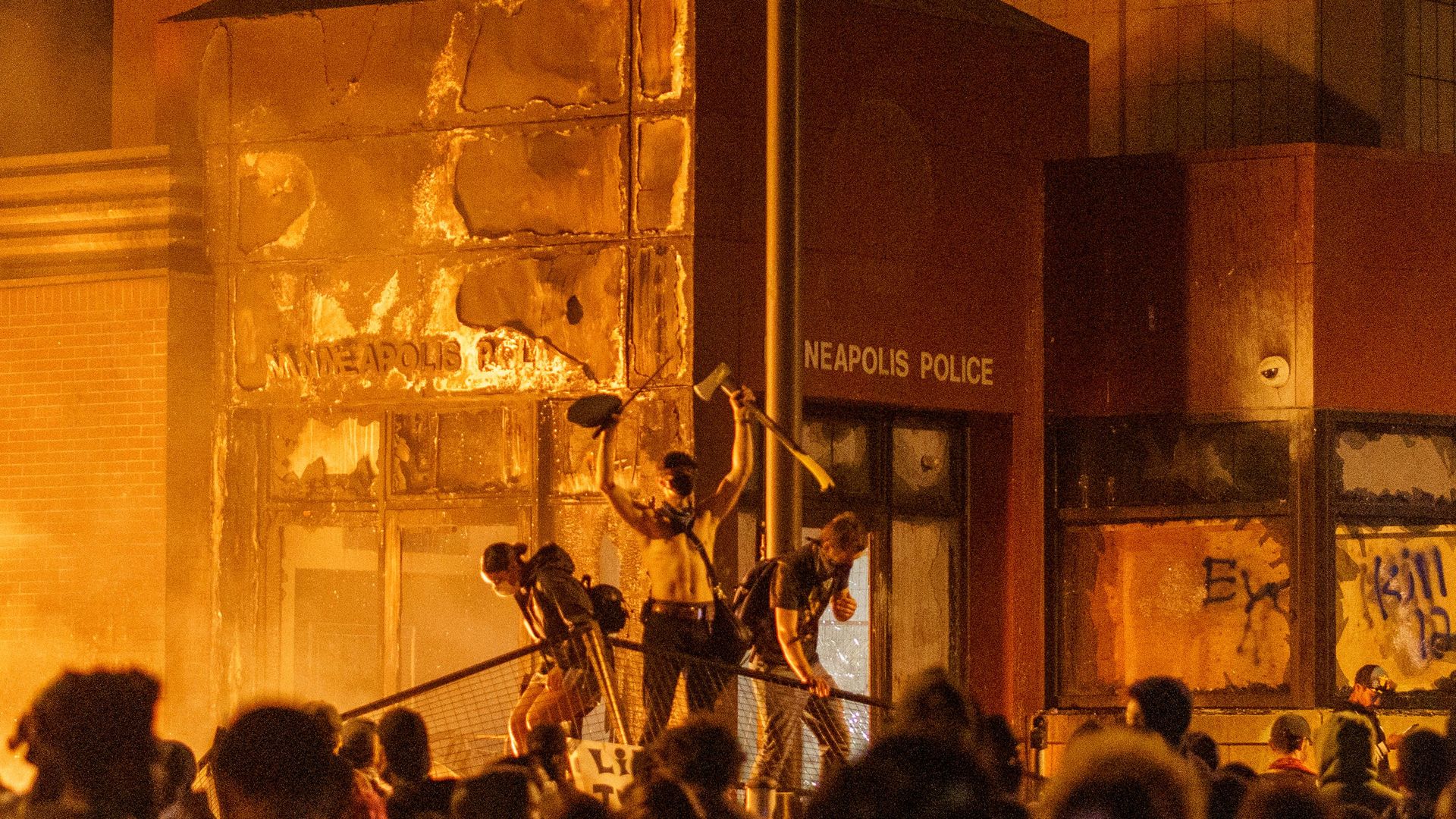 Flames from a nearby fire illuminate protesters standing on a barricade in front of the Third Police Precinct on May 28, 2020 in Minneapolis, Minnesota