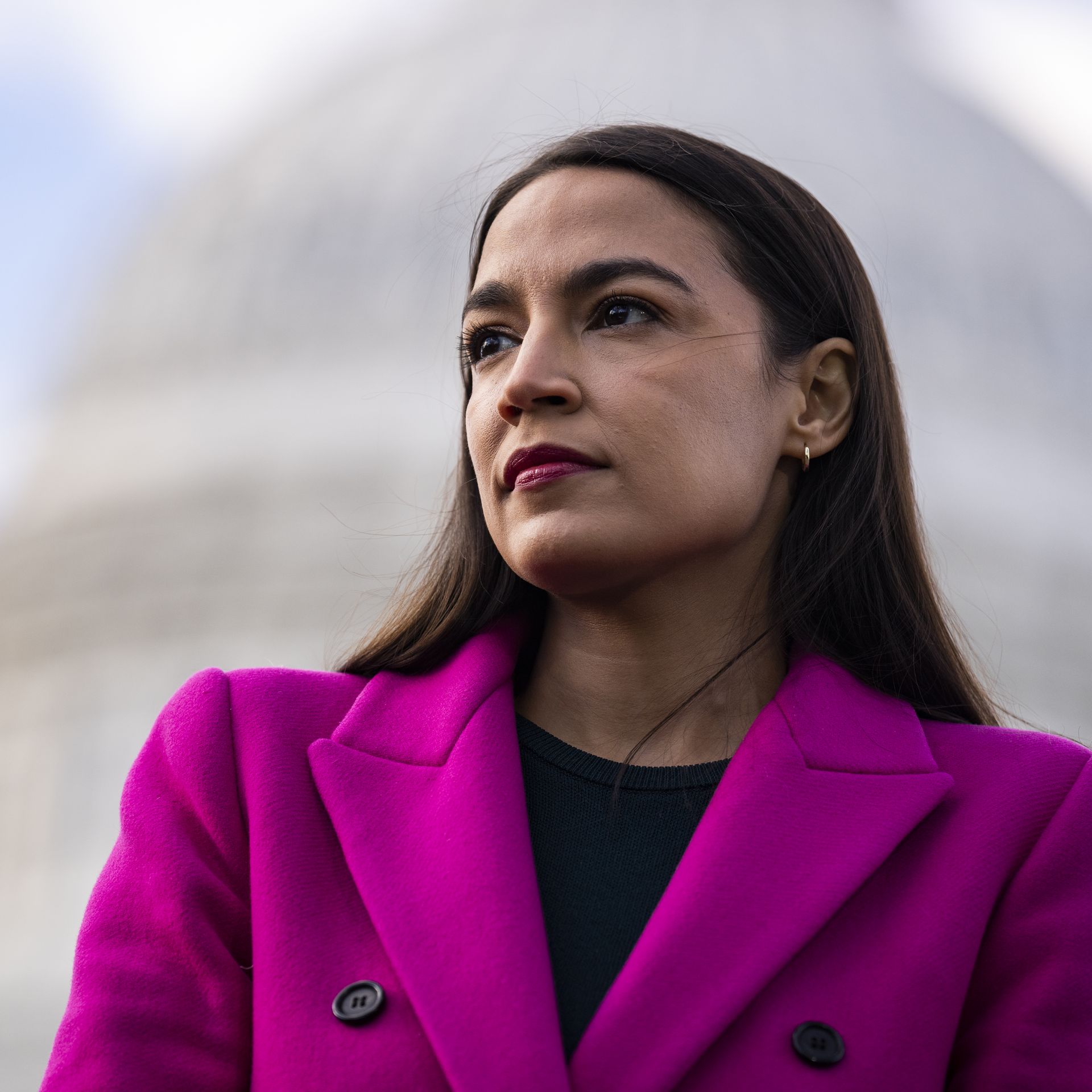 Photo of Alexandria Ocasio-Cortez in a pink coat standing outside the U.S. Capitol