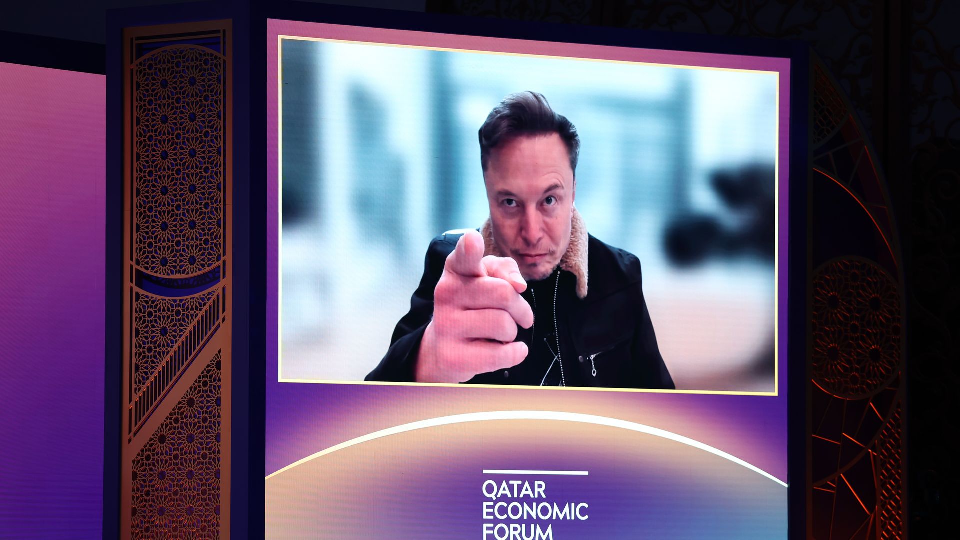 Elon Musk points as he is displayed on a screen during a virtual interview at the Qatar Economic Forum.