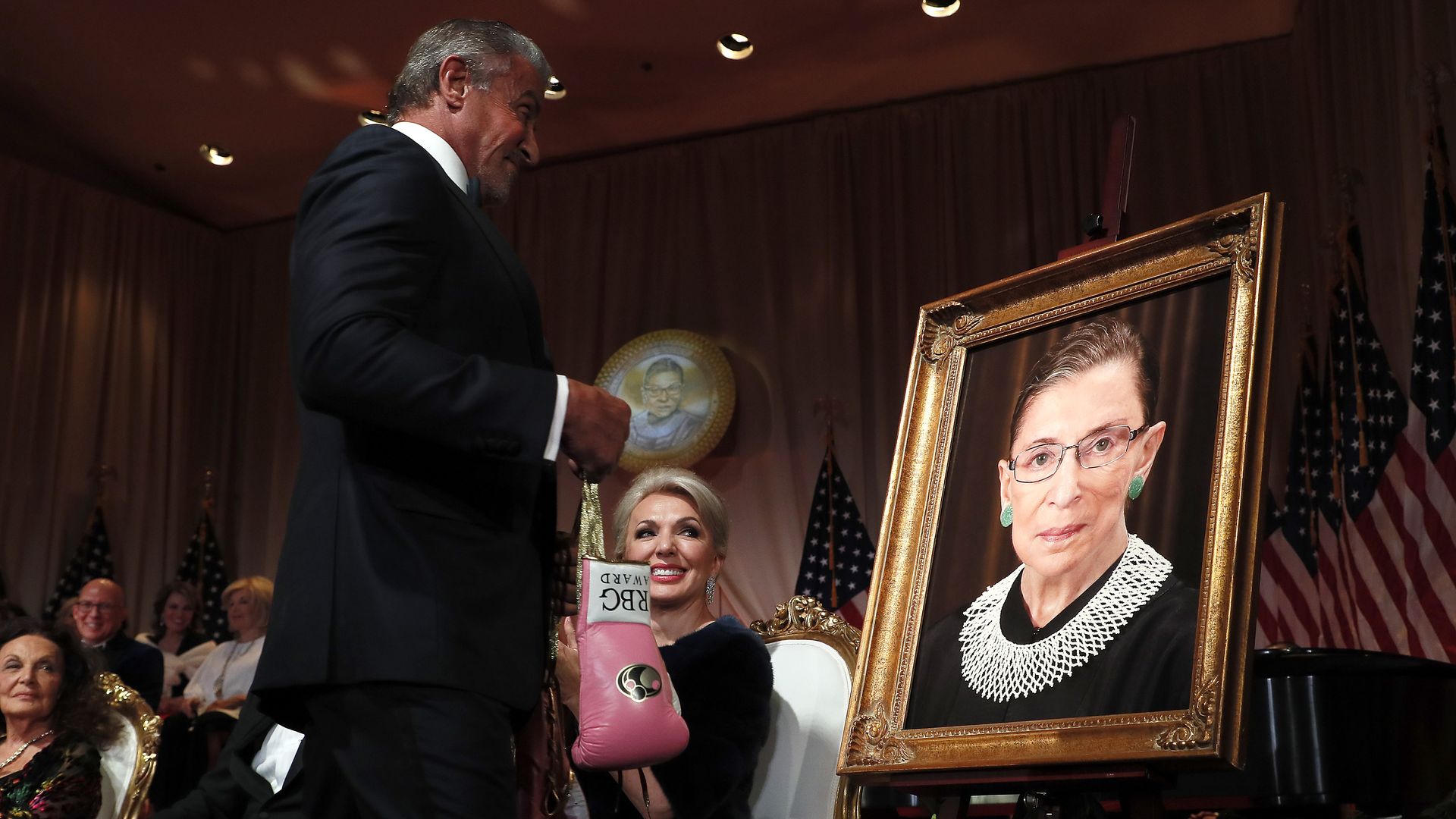 Sylvester Stallone is seen placing a pair of boxing gloves at a portrait of the late Ruth Bader Ginsburg.