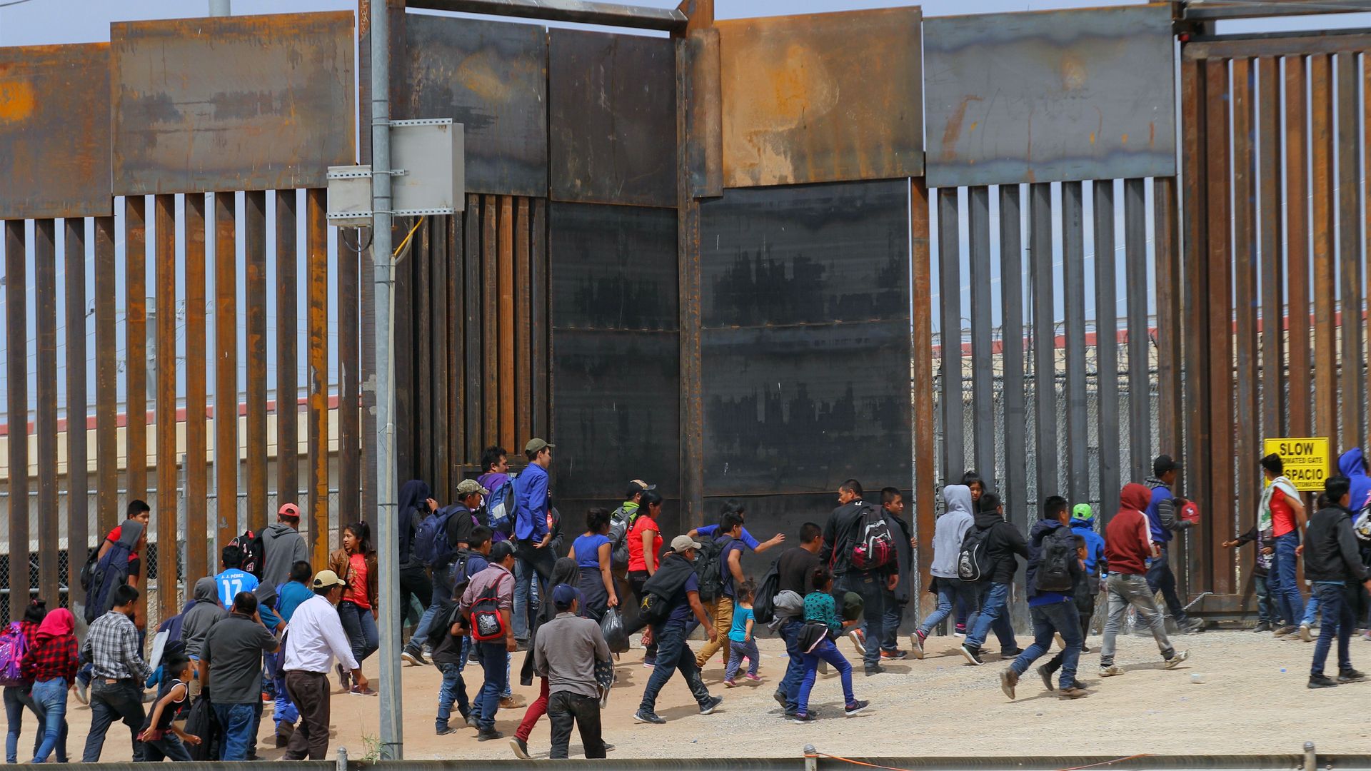 Immigrants crowding a border wall at the U.S. southern border.