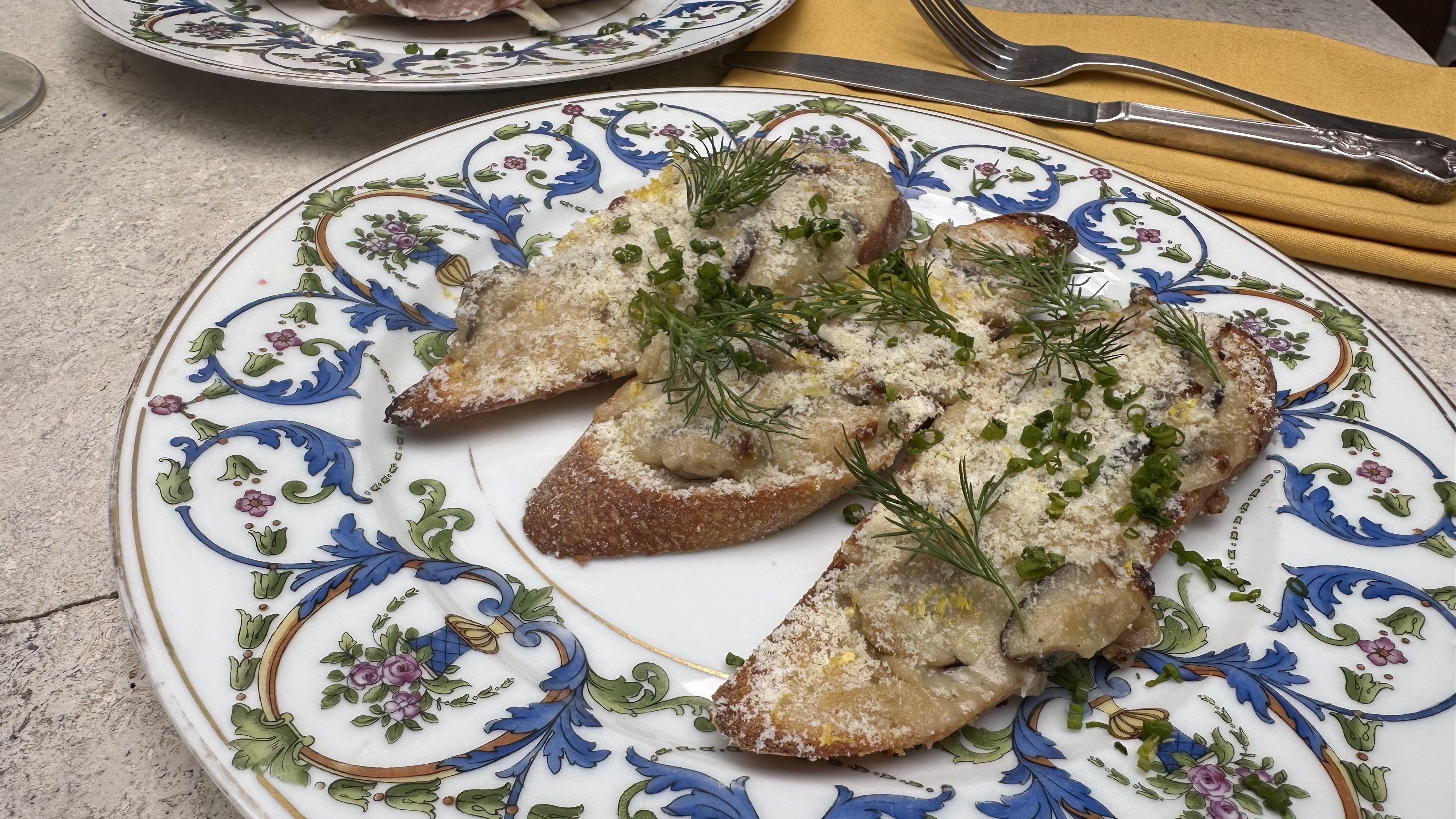 A close-up photo of three slices of toast topped with mushrooms and herbs on a plate decorated with blue florals.