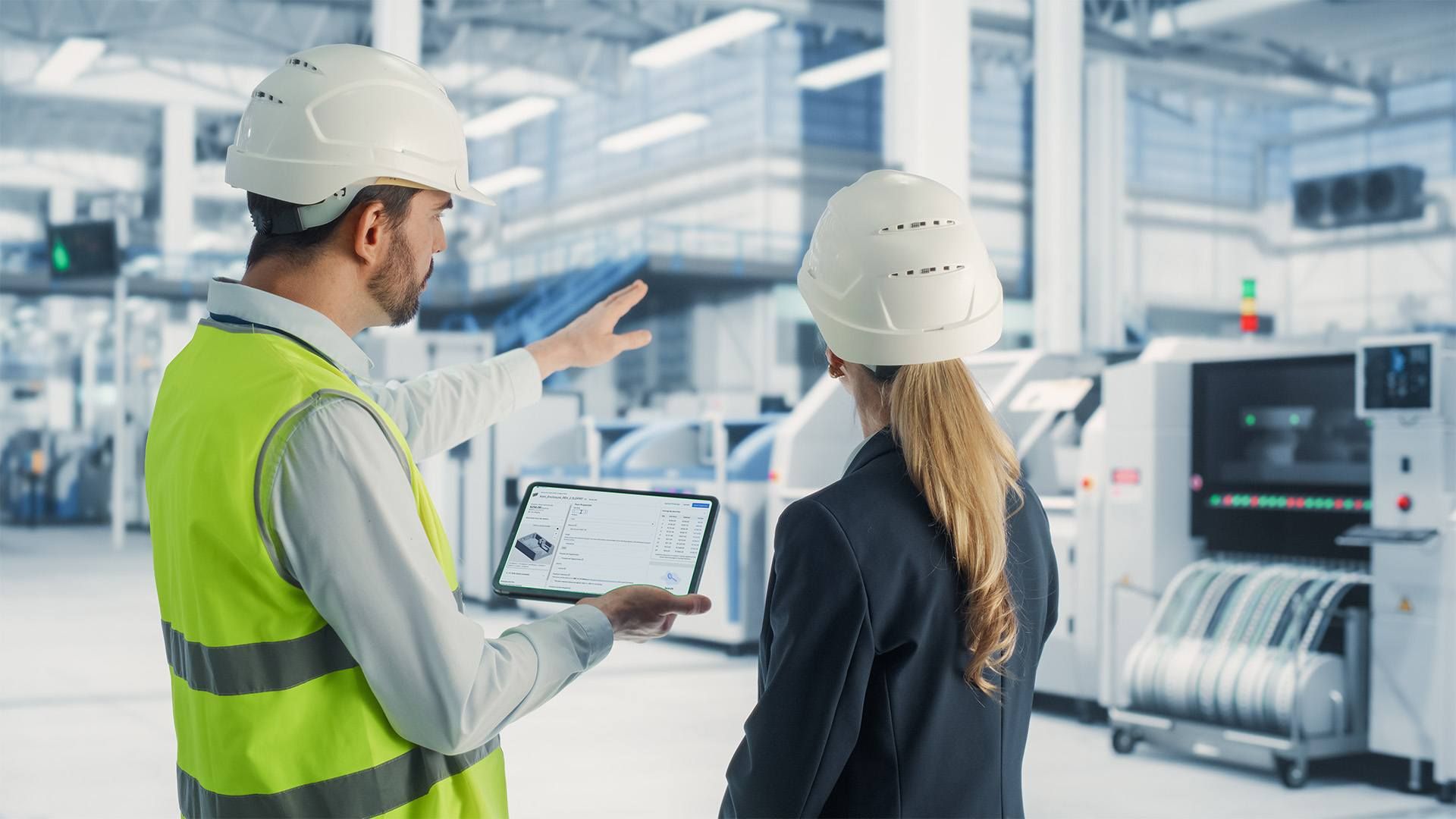 A man and a woman in hard hats survey a factory.