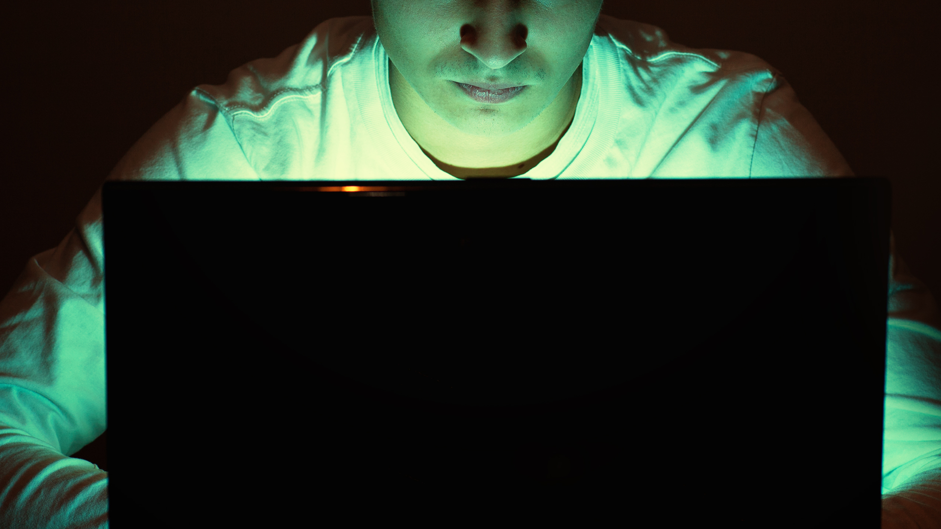 A face is lit up by a laptop monitor
