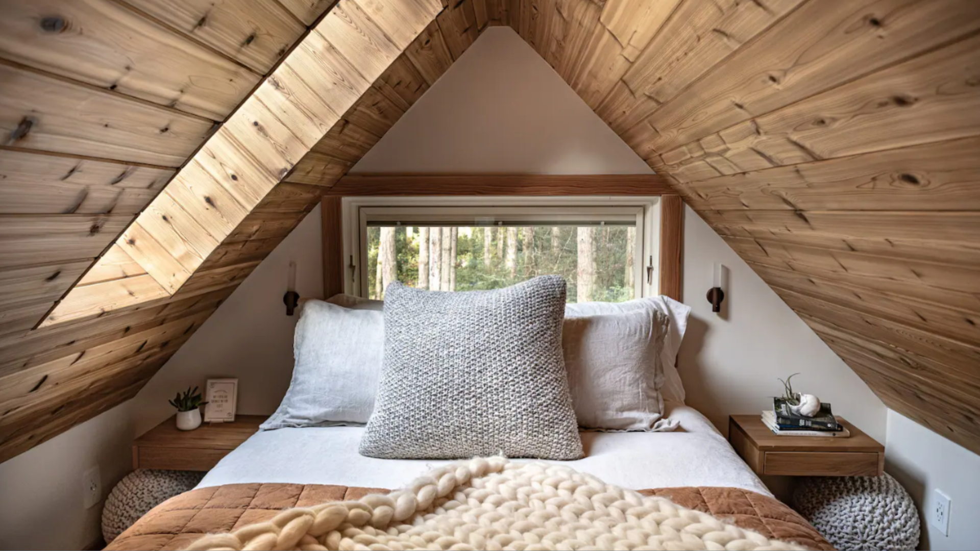 A bedroom in an Airbnb cabin with a slanted A-shaped roof. 