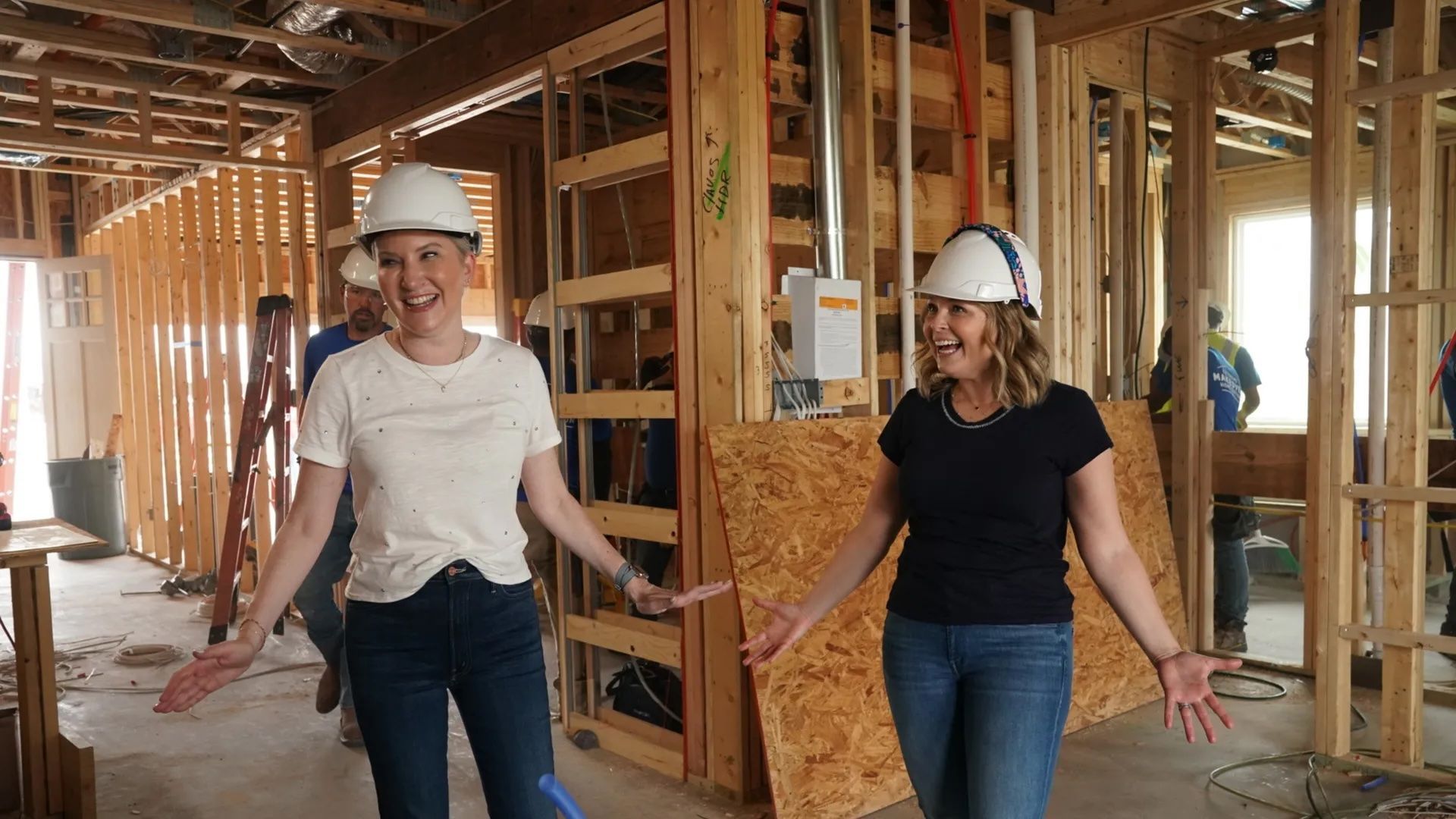 Clea Shearer and Joanna Teplin stand inside a partially constructed house while wearing white hard hats.