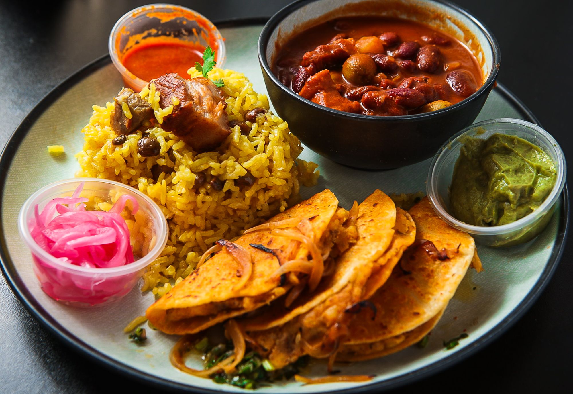 A plate of food with three tacos, rice and beans. 