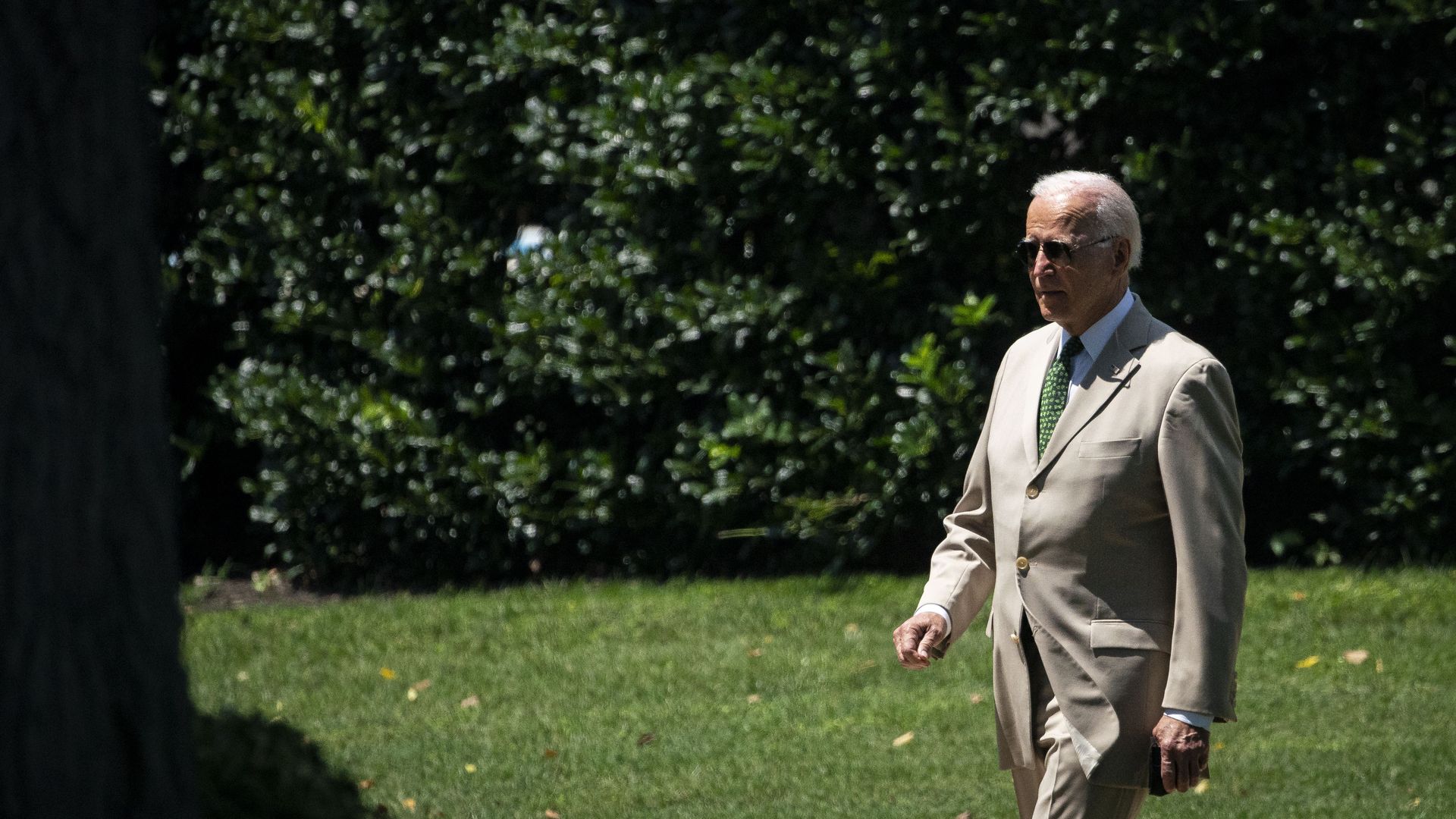 Photo of Joe Biden in a tan suit and sunglasses walking on grass