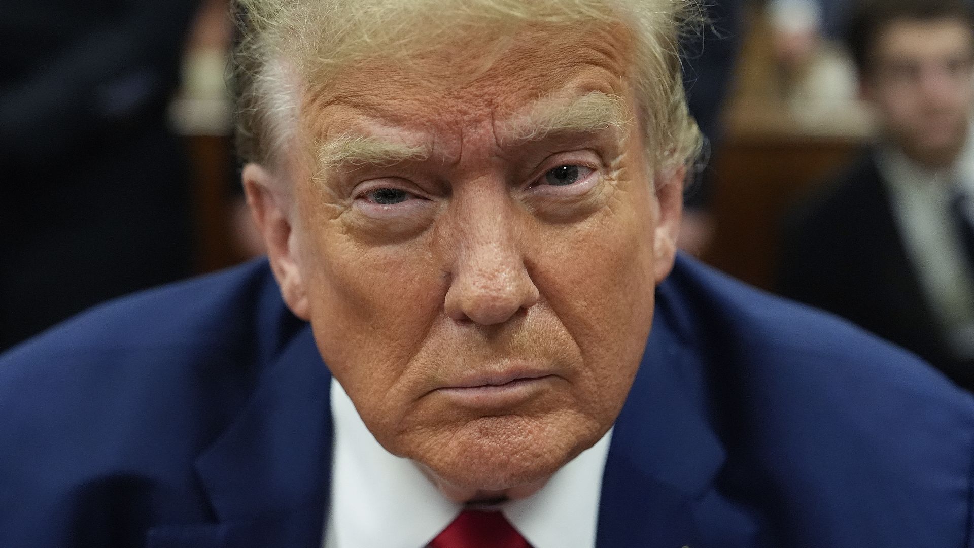 A picture of Trump in a blue suit and red tie with the background blurred.