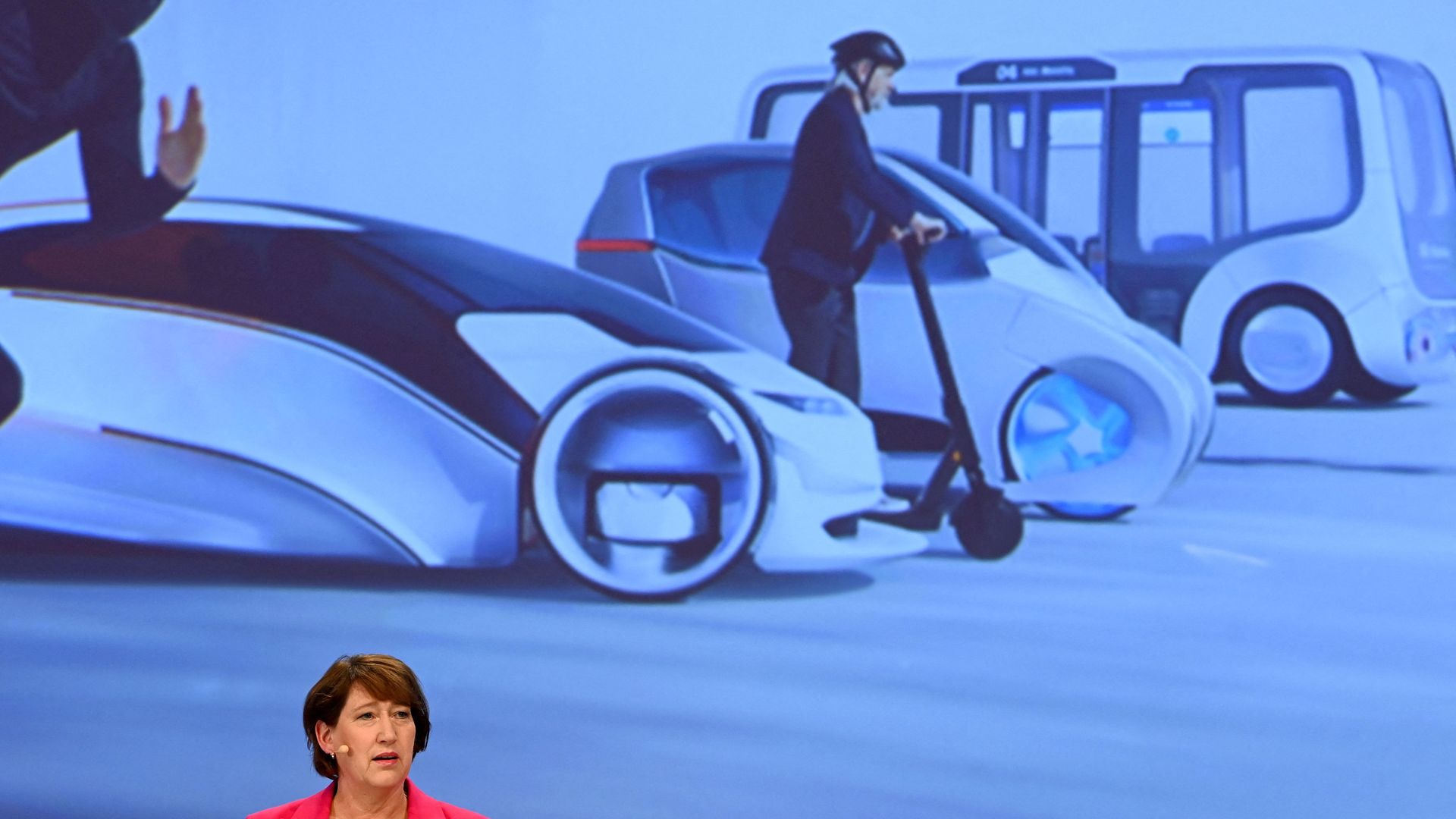 Image of Hildegard Mueller, President of the Association of the German Automotive Industry, in front of a screen demonstrating multiple modes of transportation. 