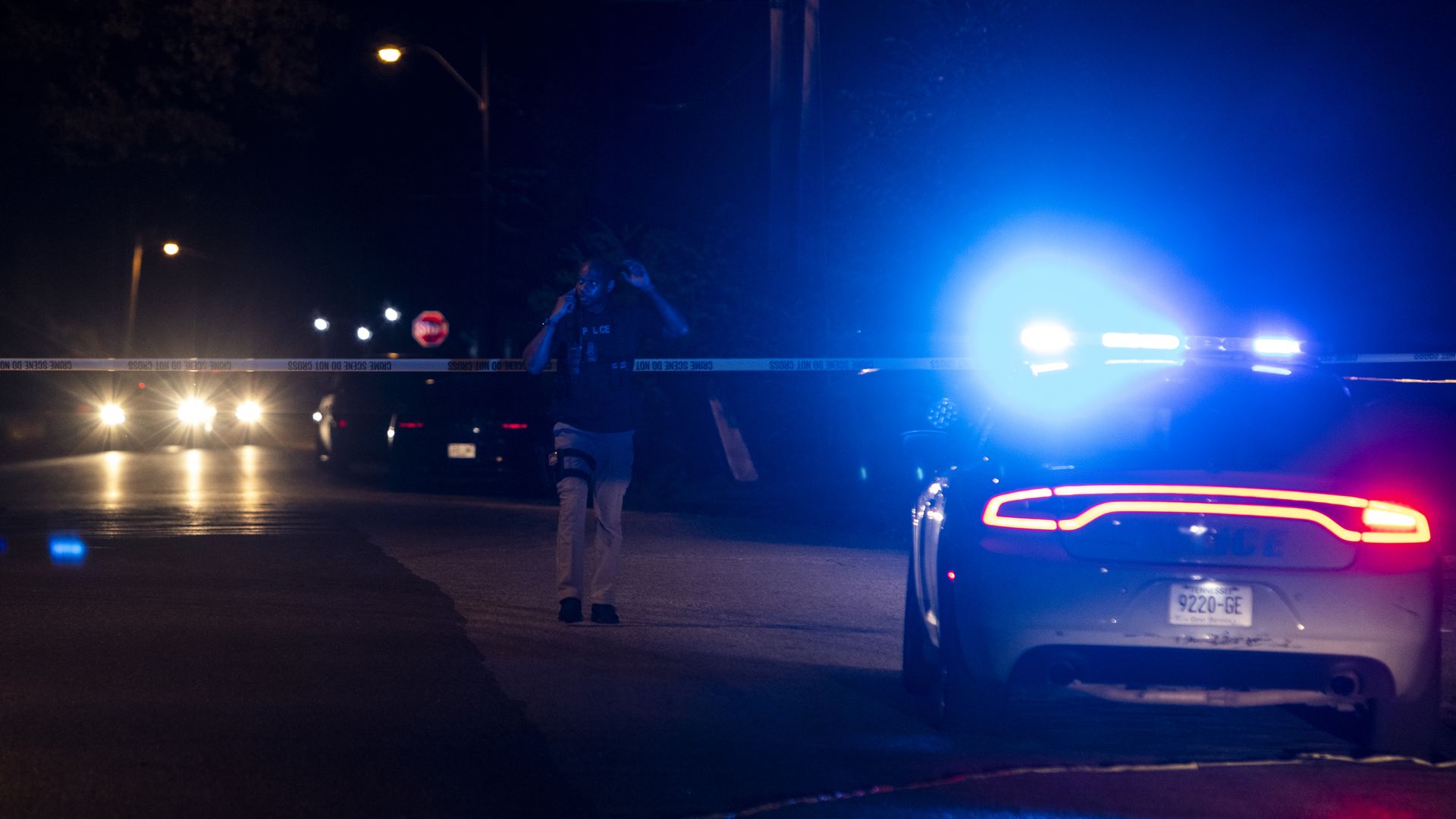 A police officer investigates at the scene at night where a man was taken into custody following a series of shootings throughout the city on September 7, 2022 in Memphis, Tenn. Police cars have lights on. 