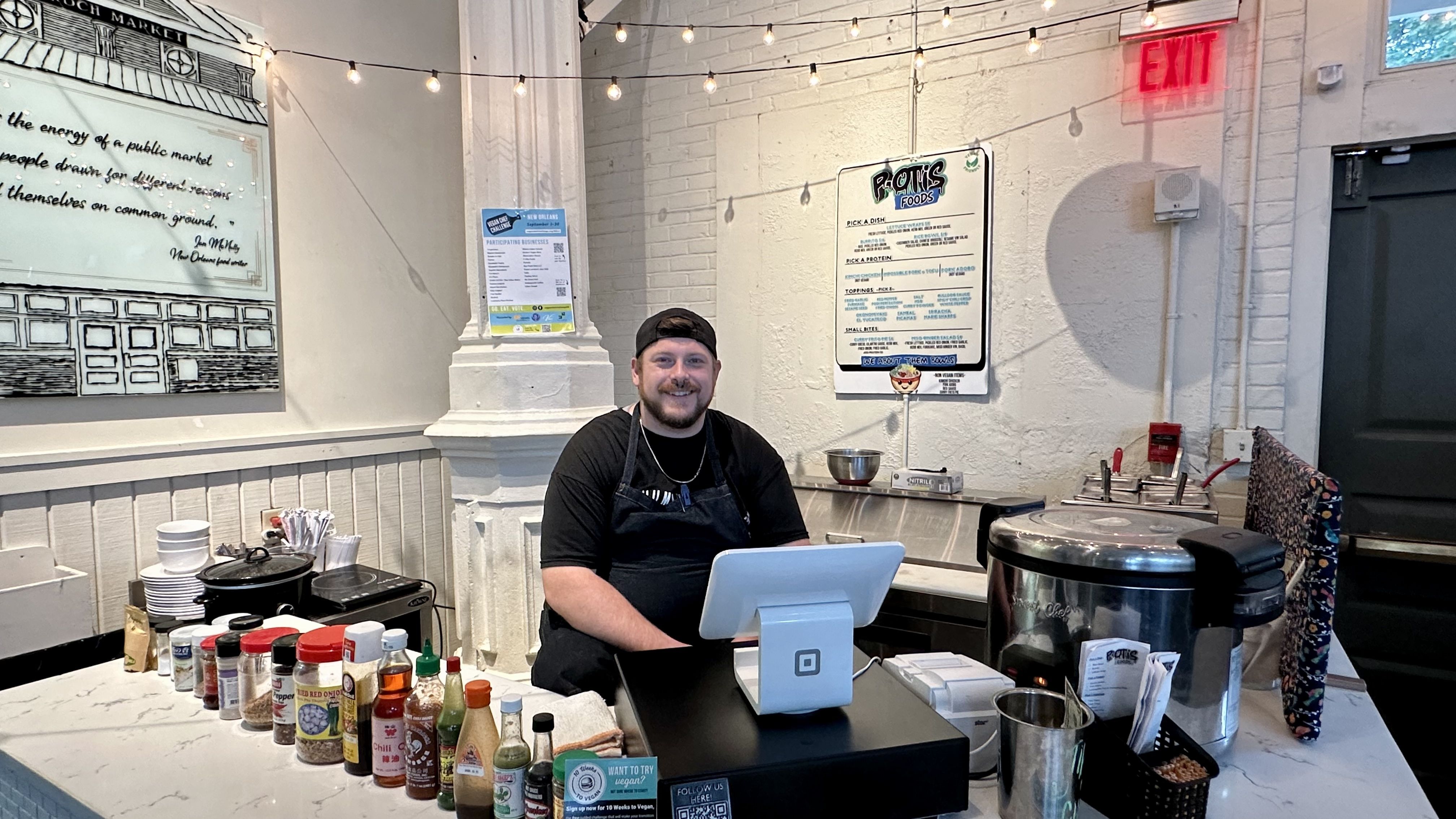 Photo shows a man sitting with hot sauces.