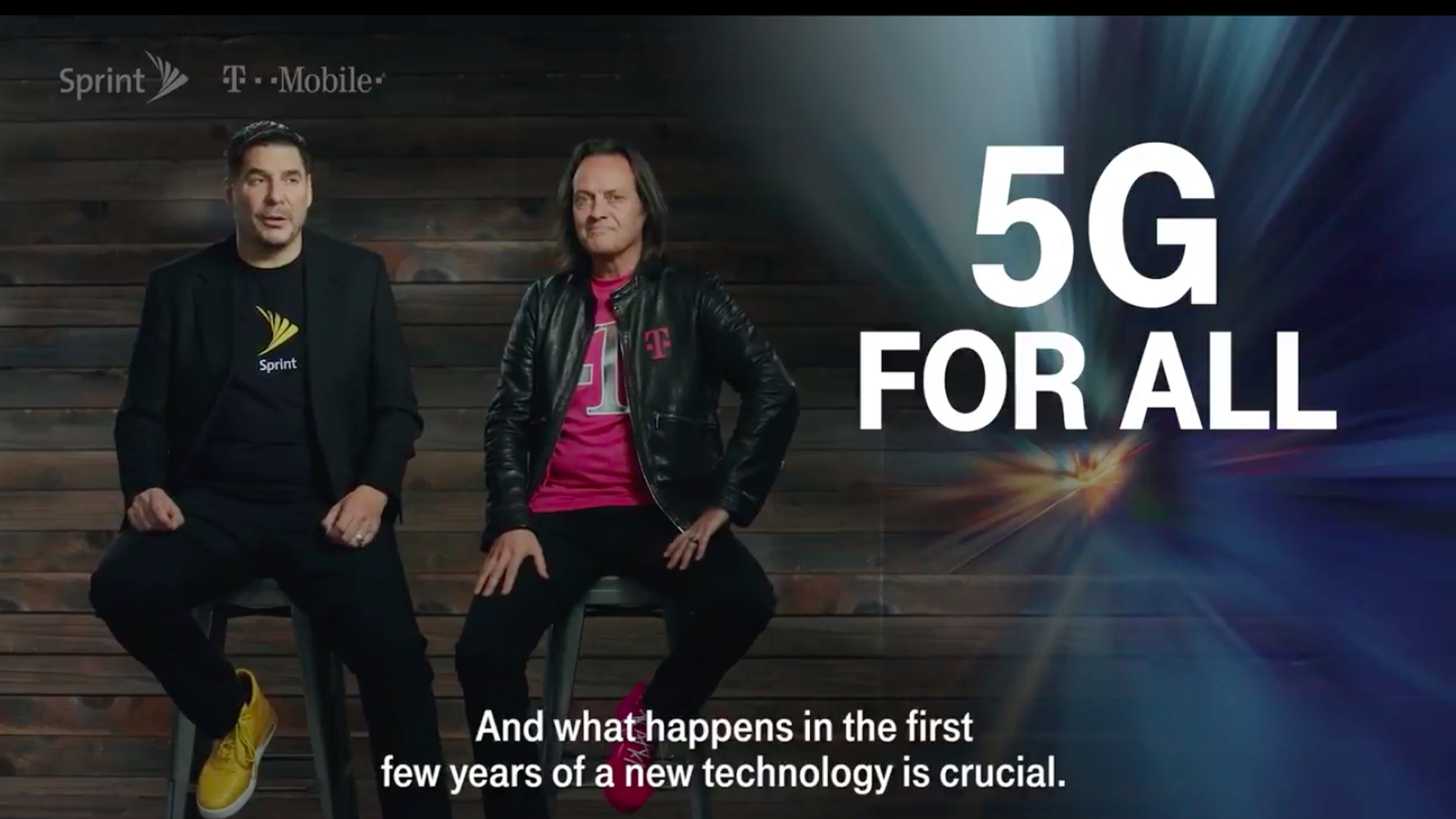 Sprint and T-Mobile CEOs sit on chairs next to a big graphic that says 5G for all