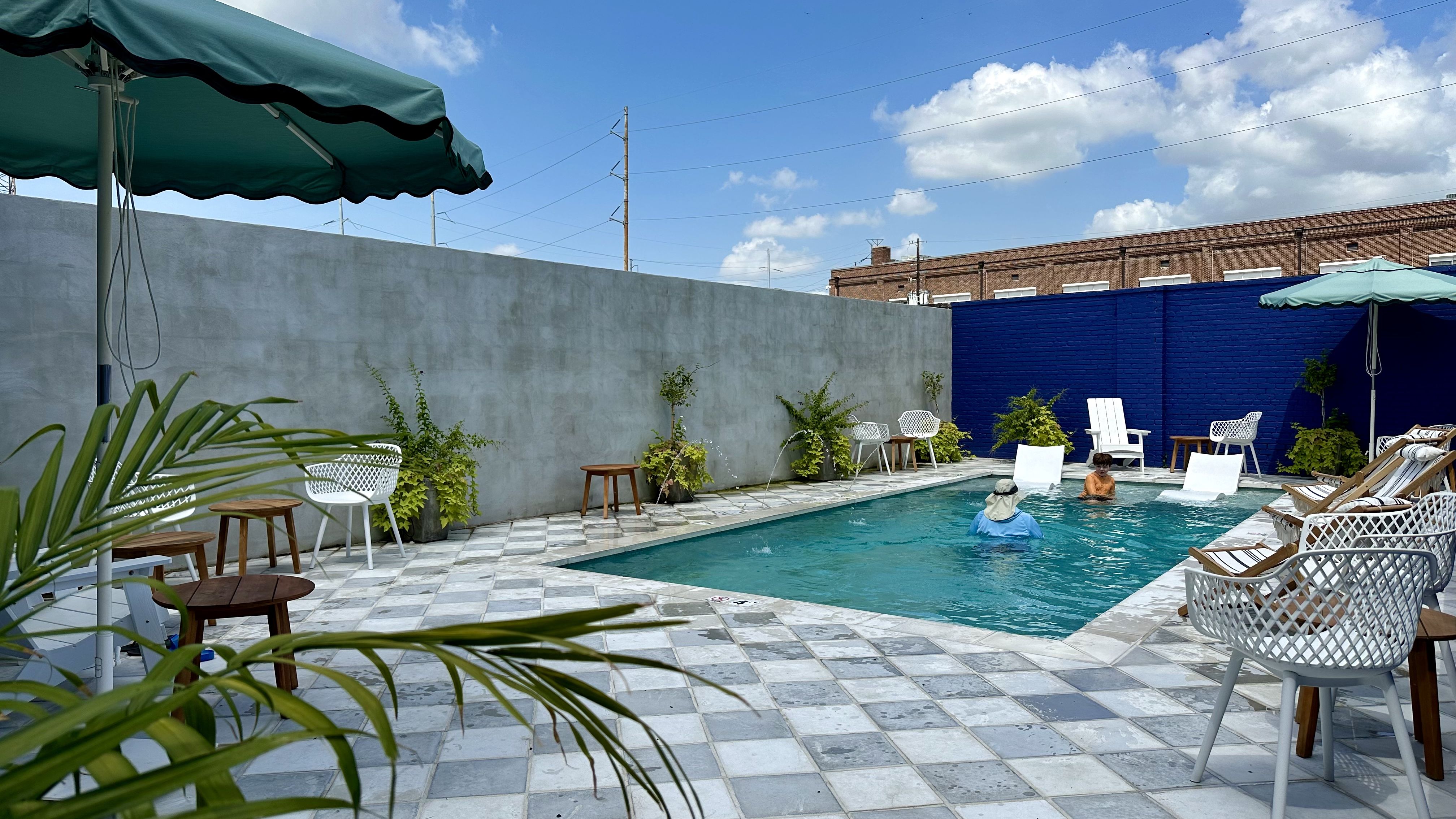 Image shows a pool with plants and chairs.