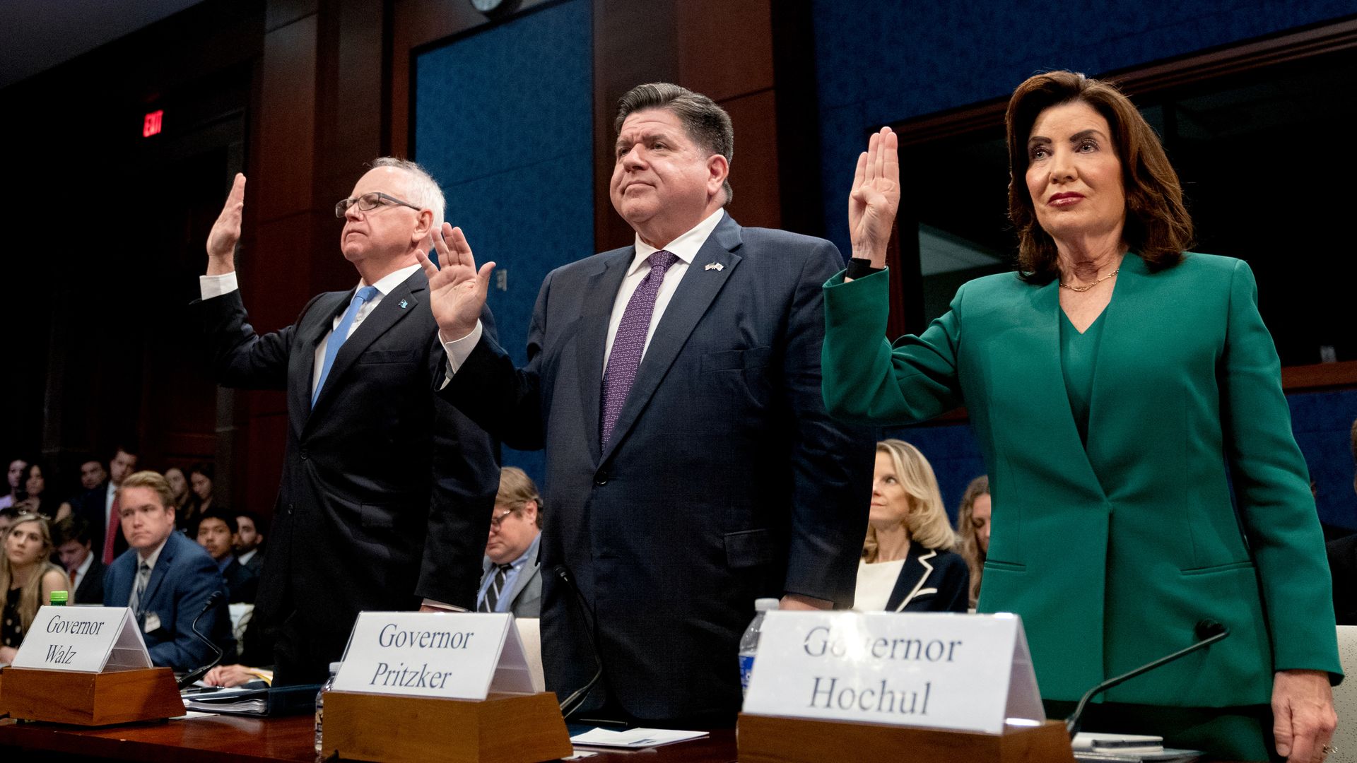 Tim Walz, JB Pritzker and Kathy Hochul stand with their right hands elevated as they are sworn in during hearing 
