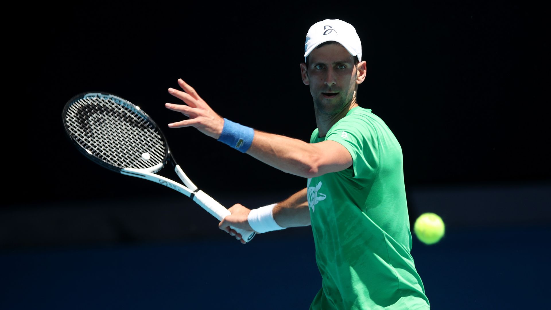 Photo of Novak Djokovic with his racket swung behind him as a tennis ball approaches