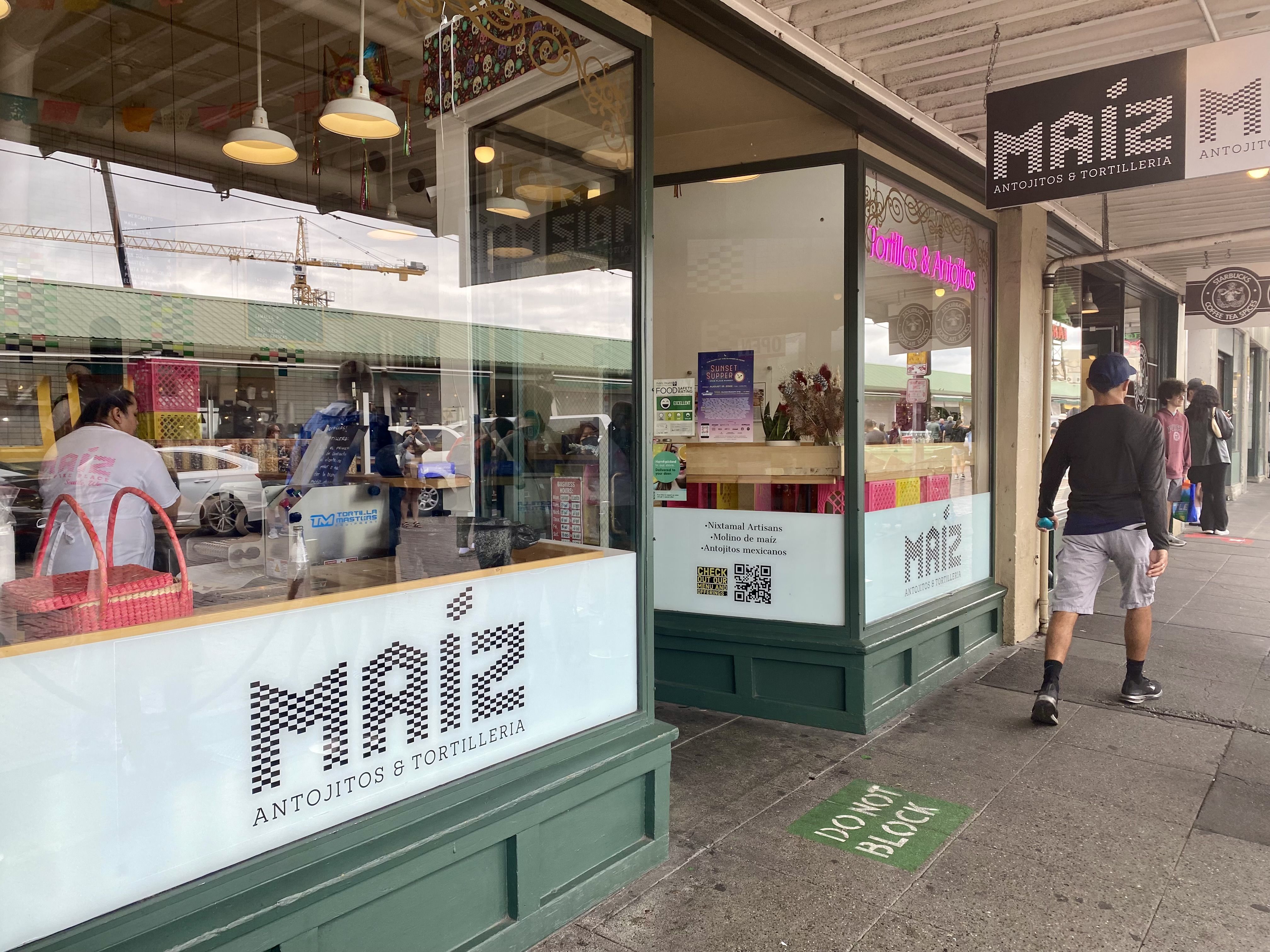 A storefront that says "Maiz" on the window, with someone walking by along the sidewalk.